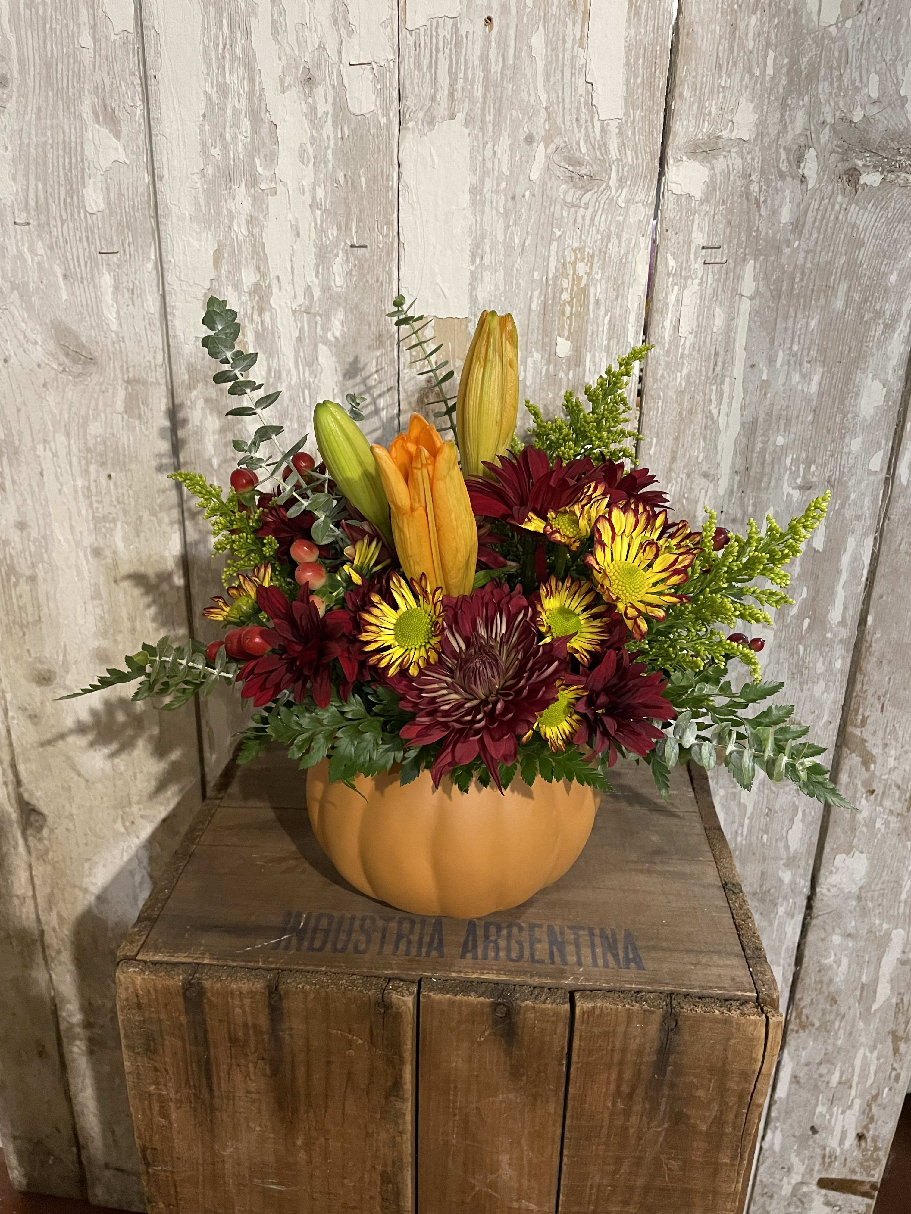 Autumn floral arrangement in a pumpkin-shaped container with lilies and mums