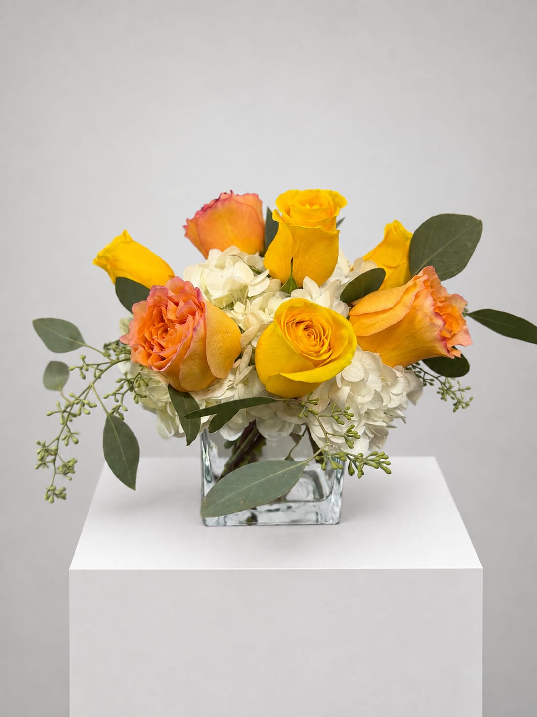 Yellow and peach roses arranged in a square glass vase