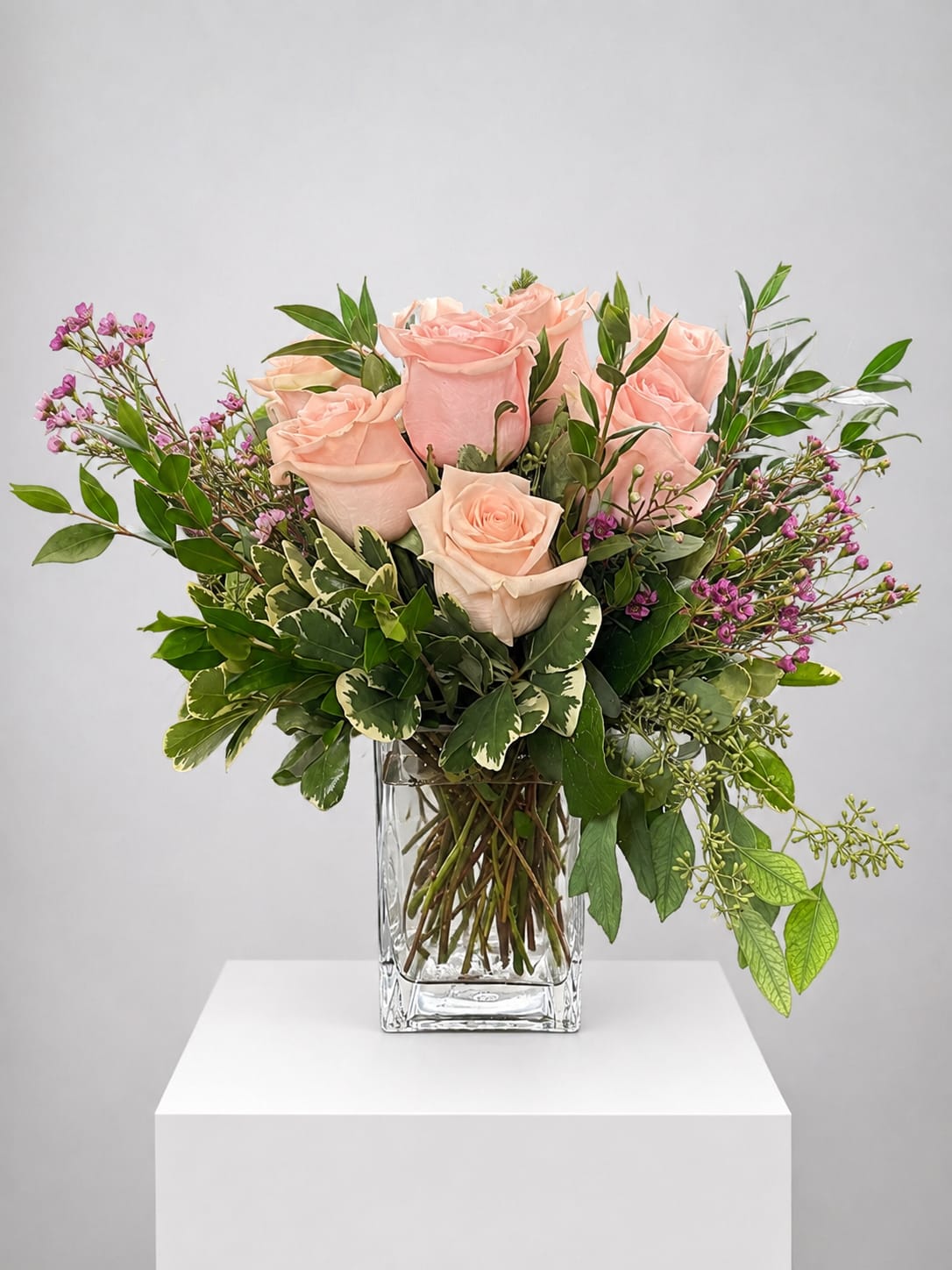 Blush pink roses in a clear glass vase with mixed greenery