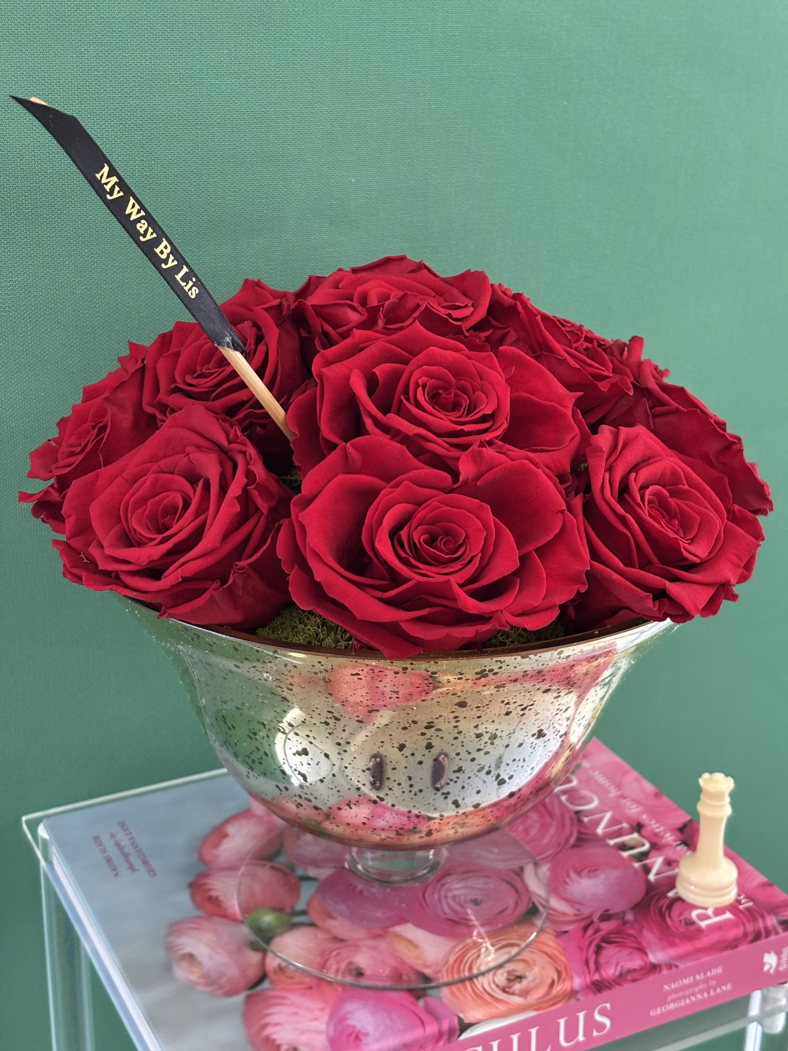 Red roses arranged in a silver pedestal bowl with a black ribbon pick