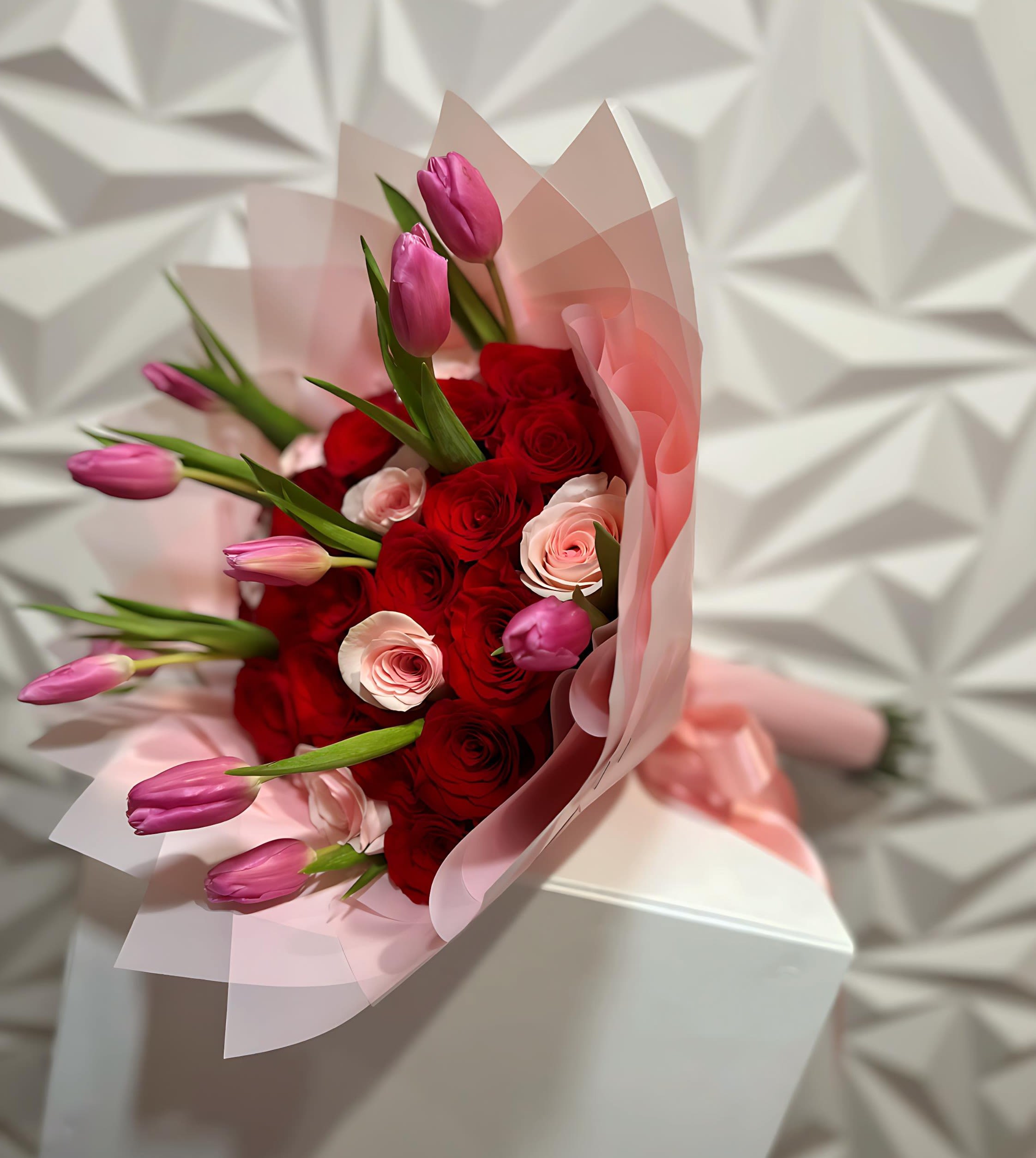 Bouquet of red roses and pink tulips wrapped in pale pink paper