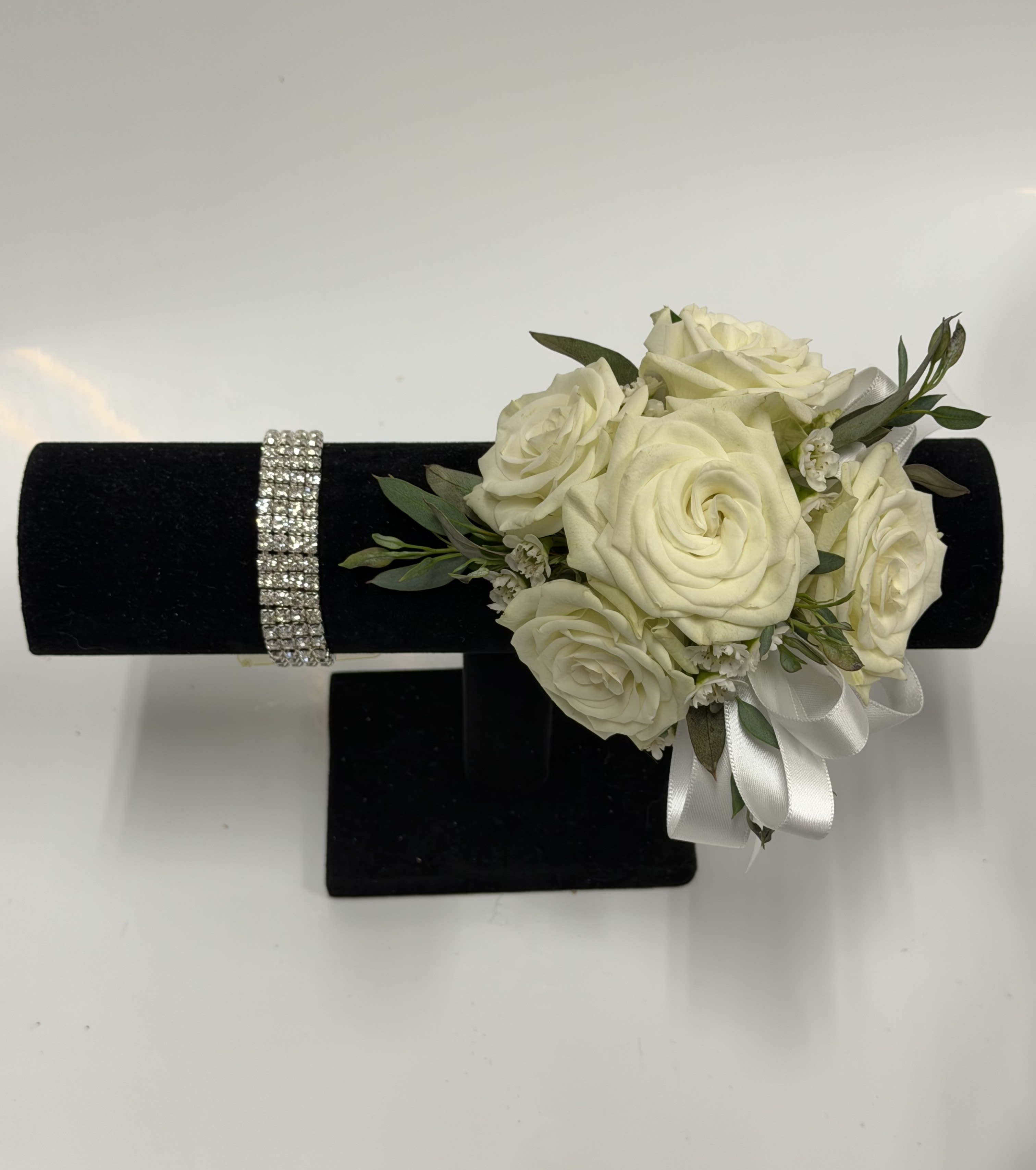 White Spray Rose Corsage with Silver Rhinstone Wristlet - White spray roses, sheer ribbon, pearl band, white or light pink filler flower on a bed of greenery. Ribbon color can be customized; please specify in the pick-up note section.