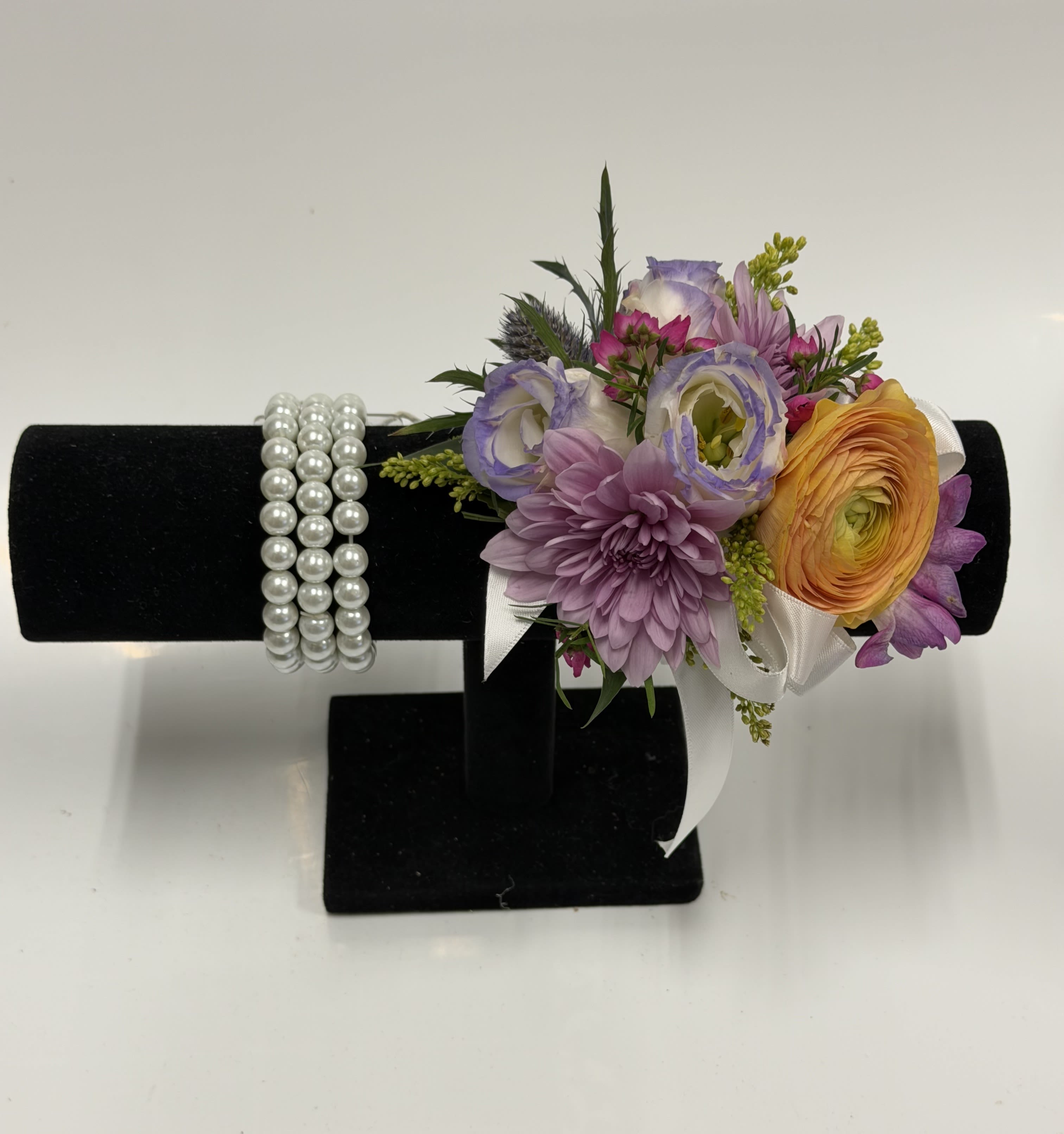 COLORFUL ENGLISH GARDEN CORSAGE WITH PEARL WRISTLET - Ranunculus, lisianthus, and a variety of other flowers in soft spring colors, accented with filler and greenery on a pearl beaded band. Ribbon color can be customized; please specify in the pick-up note section. ***Will NOT be identical to photo***