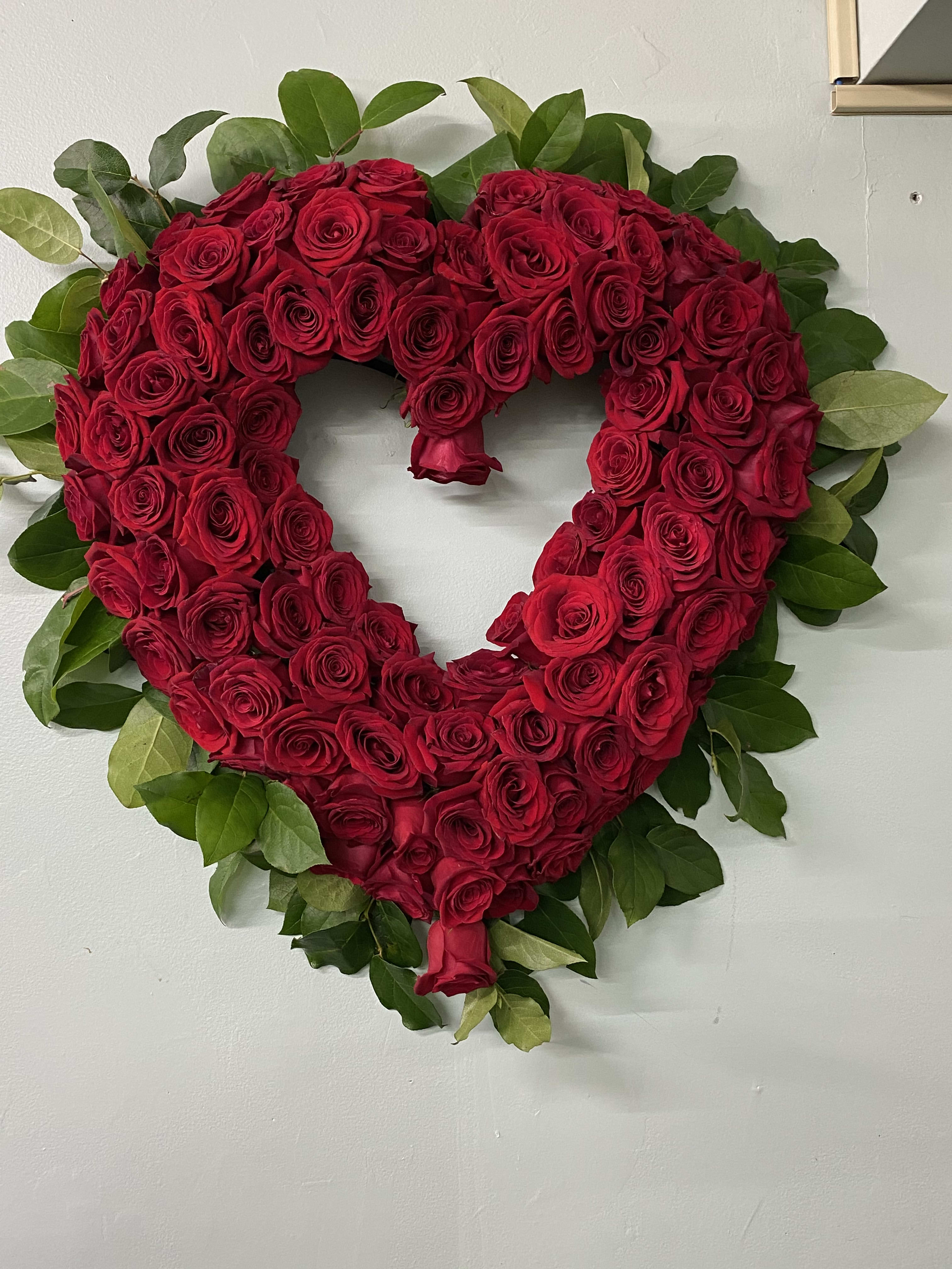 Heart-shaped arrangement of red roses with green foliage