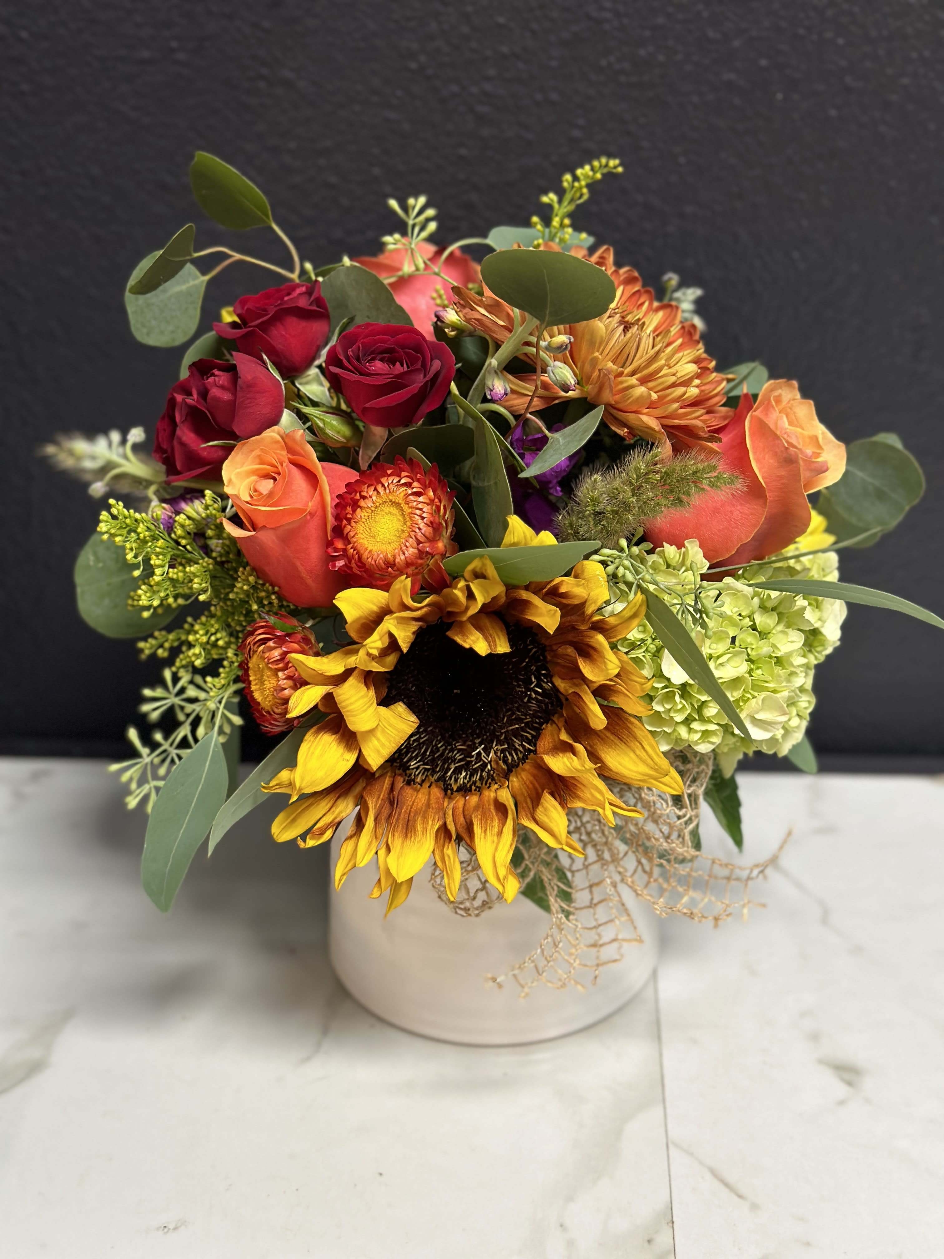 Mixed bouquet with sunflowers, roses, and hydrangea in a white vase