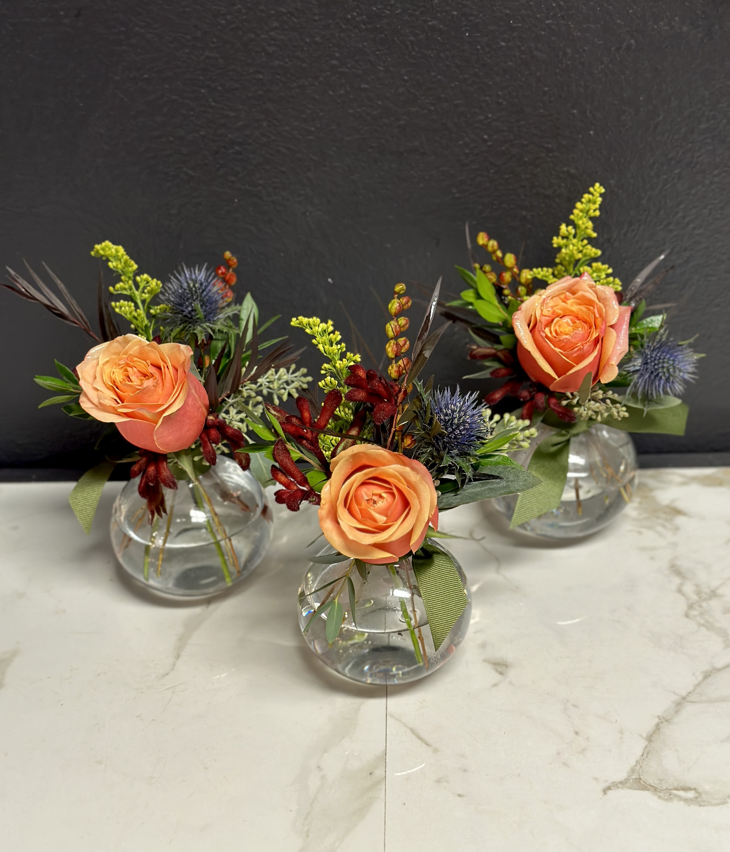 Three small floral arrangements in round glass vases with peach roses