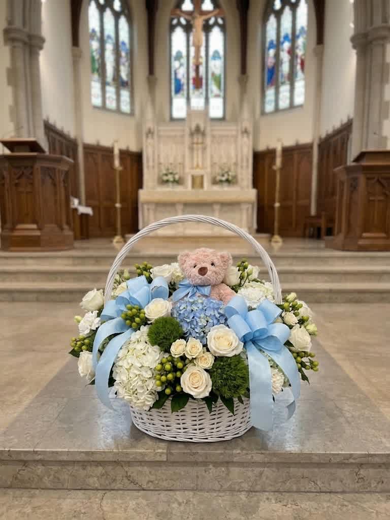 White flower basket with blue ribbons and a teddy bear in a church