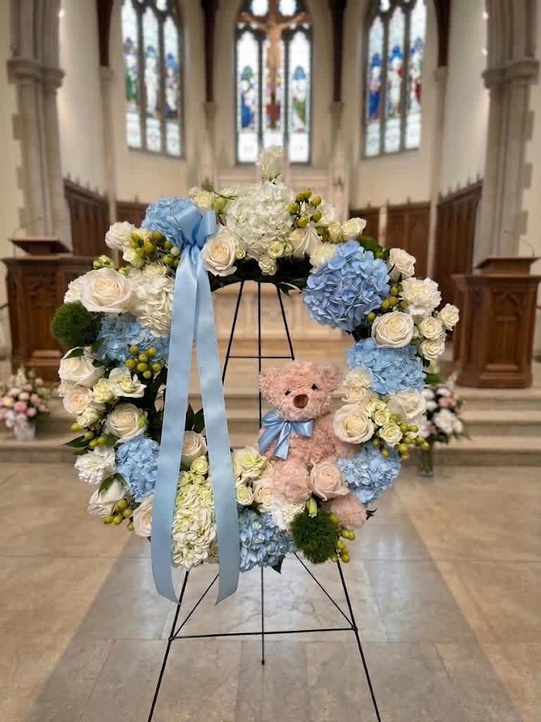 Floral wreath with blue ribbon and teddy bear in a church setting