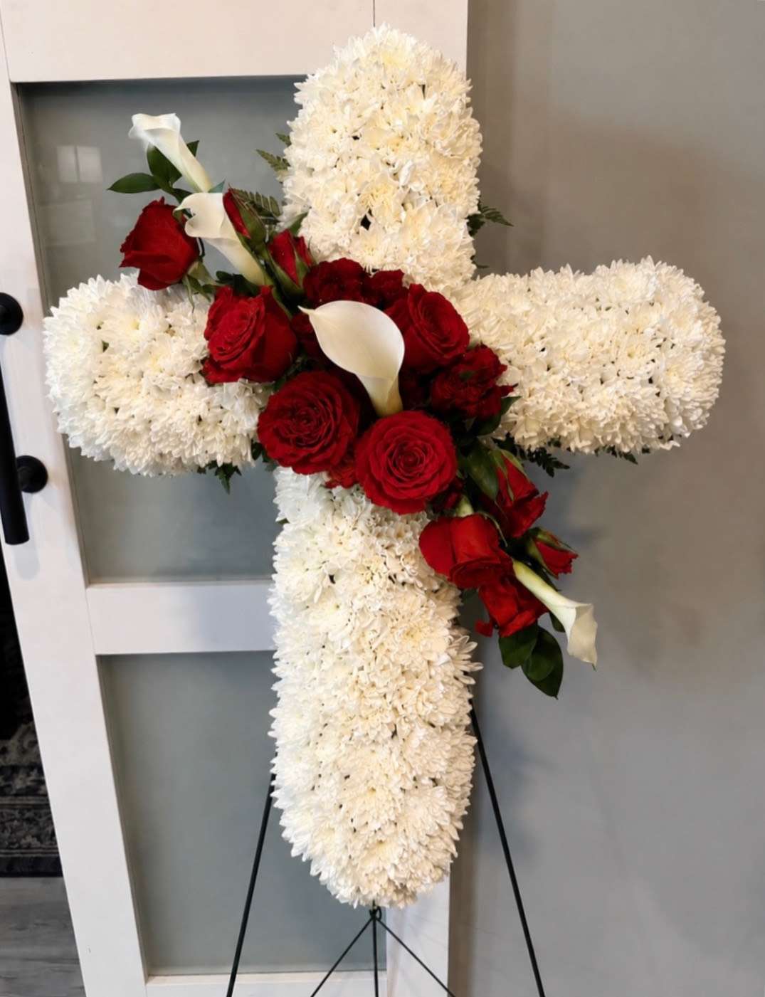 Cross-shaped floral tribute with white chrysanthemums, red roses, and white calla lilies