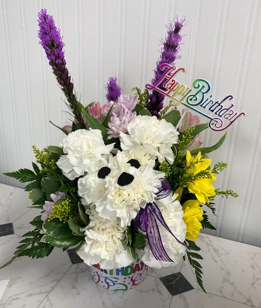 Dog-gone Birthday! - Celebrate their special day with a gift that's sure to make them smile! Dog-Gone Birthday! features an adorable puppy crafted from white carnations sitting in front of a cheerful mix of fresh lavender, white, pink, and yellow blooms. Arranged in a festive container decorated with colorful confetti and "Happy Birthday," this design is topped with a coordinating Happy Birthday pick for an extra celebratory touch. Perfect for dog lovers of all ages, this playful arrangement is a fun and unforgettable way to send birthday wishes.