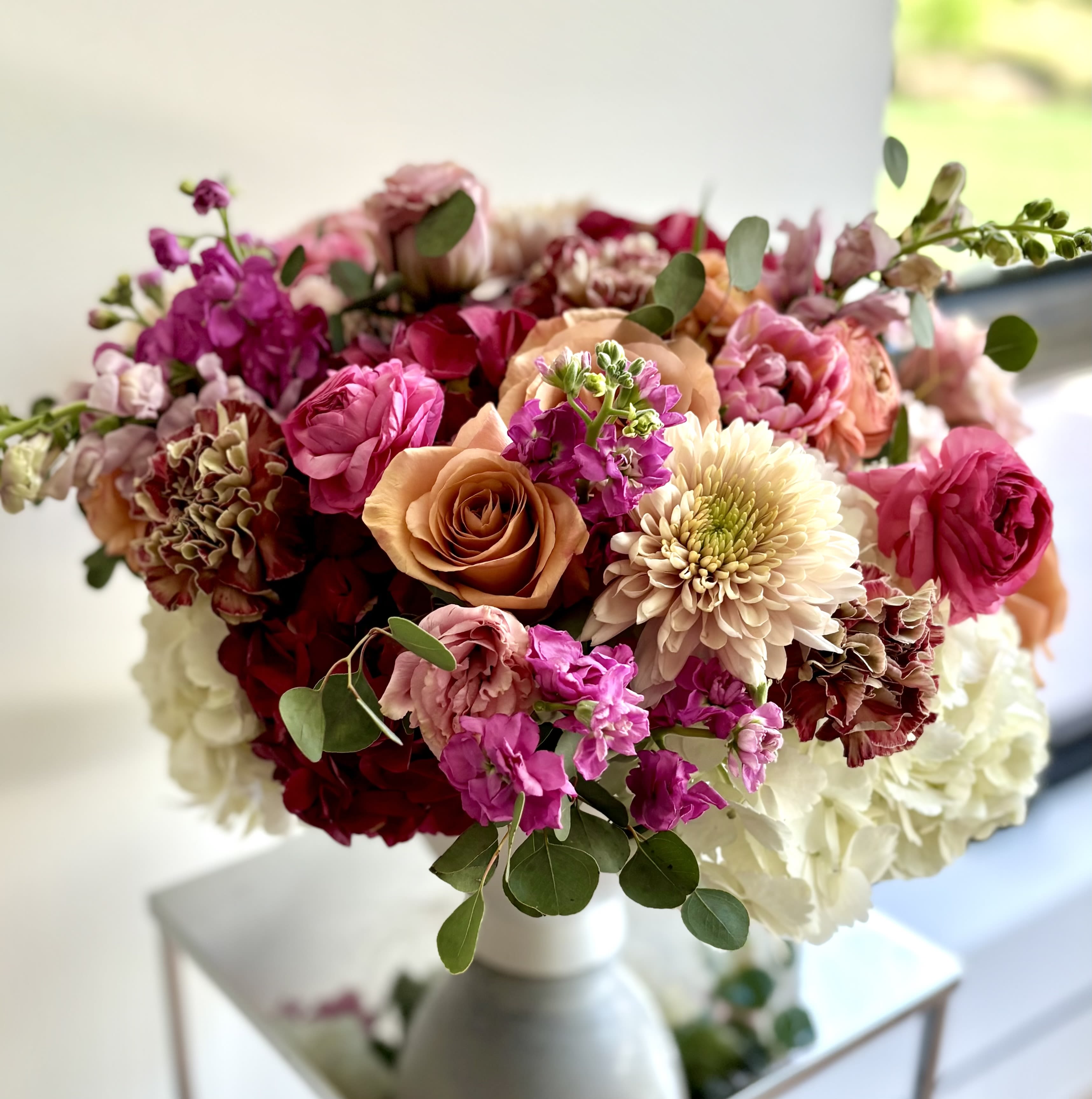 Mixed bouquet of pink, peach, and white flowers in a white vase