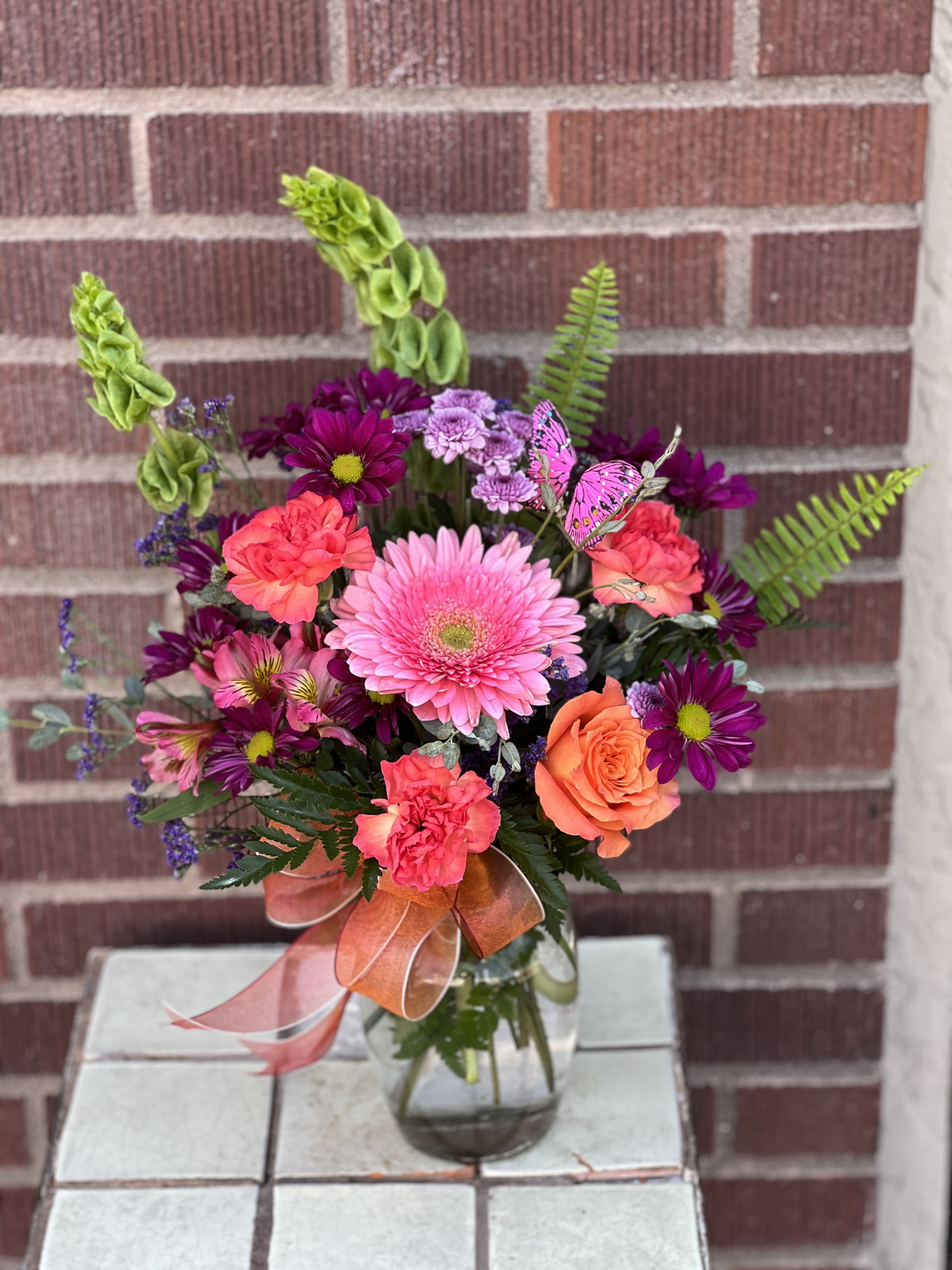 Mixed pink, purple, and orange flowers in a glass vase with a ribbon