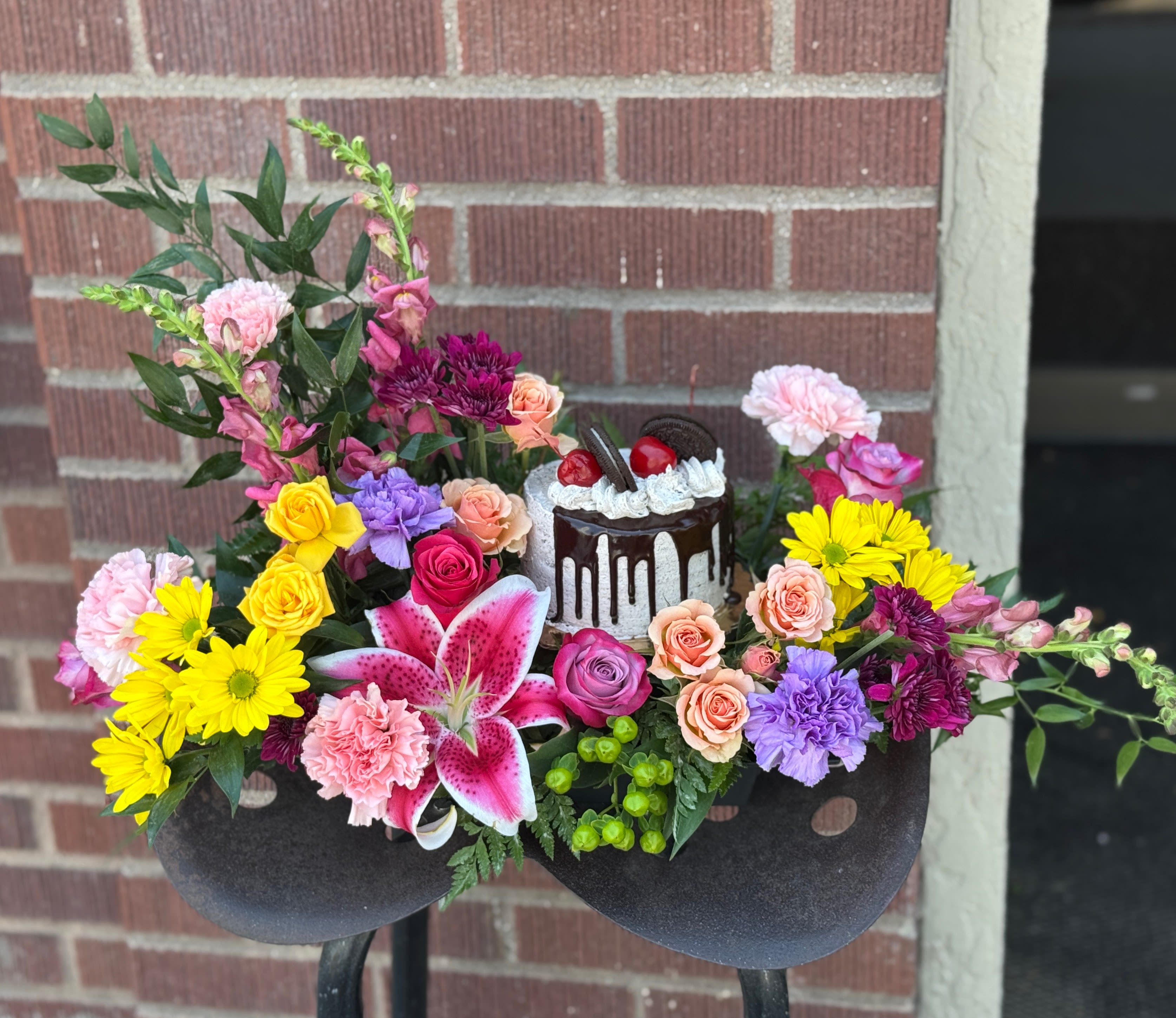 Colorful floral arrangement with a small cake centerpiece in a black container