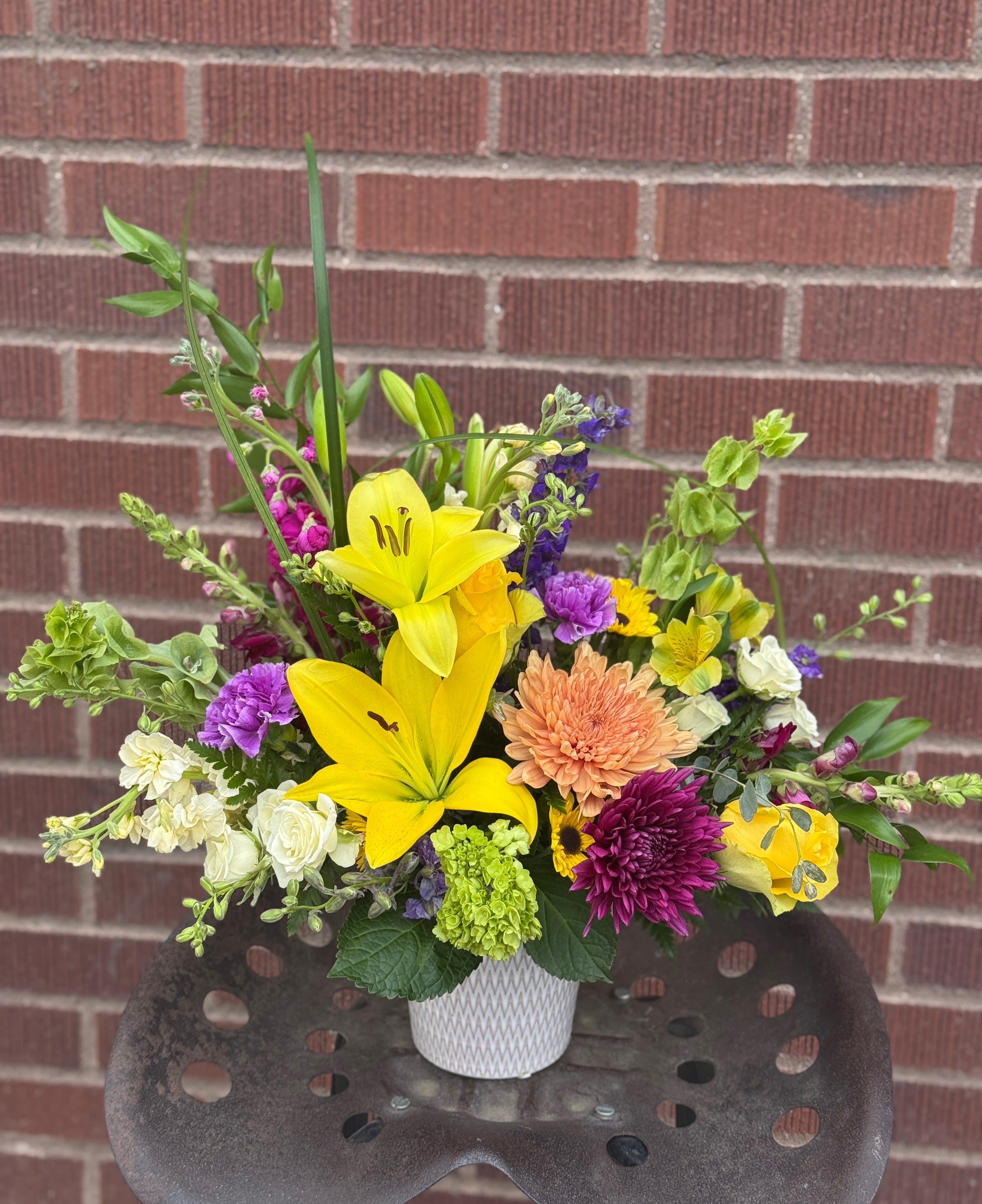 Mixed bouquet with yellow lilies, purple blooms, and a white vase