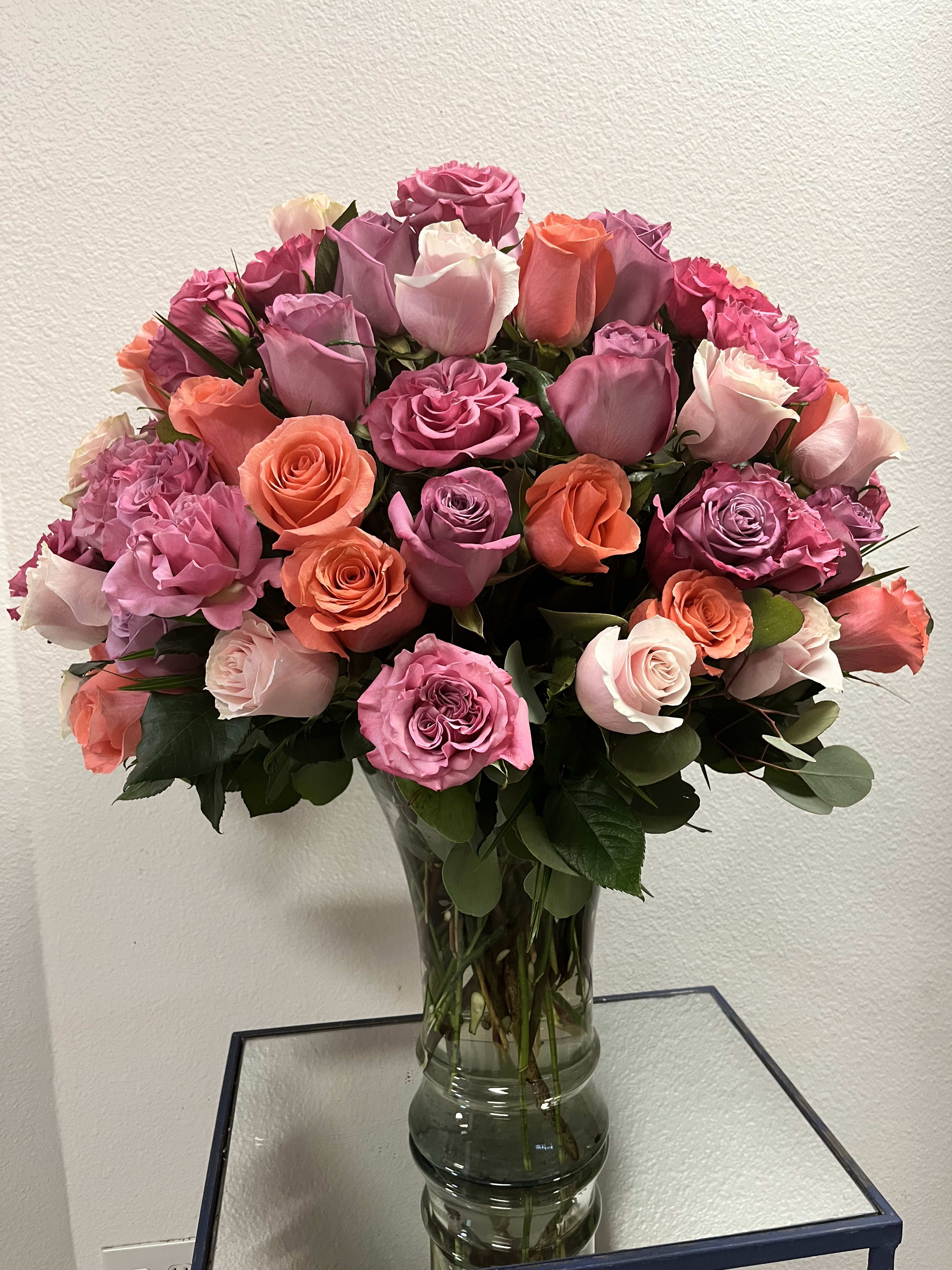 Bouquet of pink, lavender, and coral roses in a clear glass vase