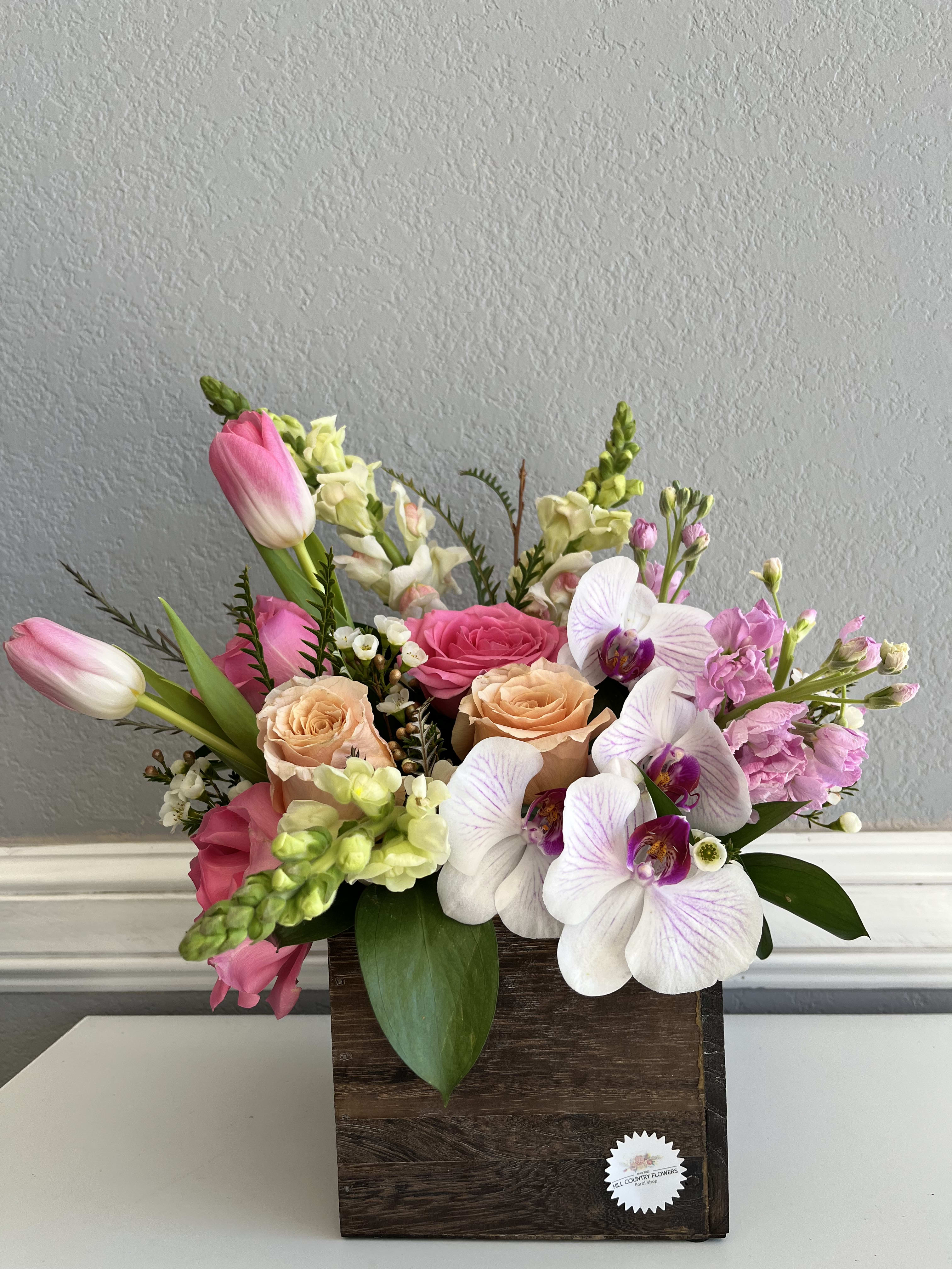 Mixed bouquet in a wooden box with pink tulips, roses, and white orchids