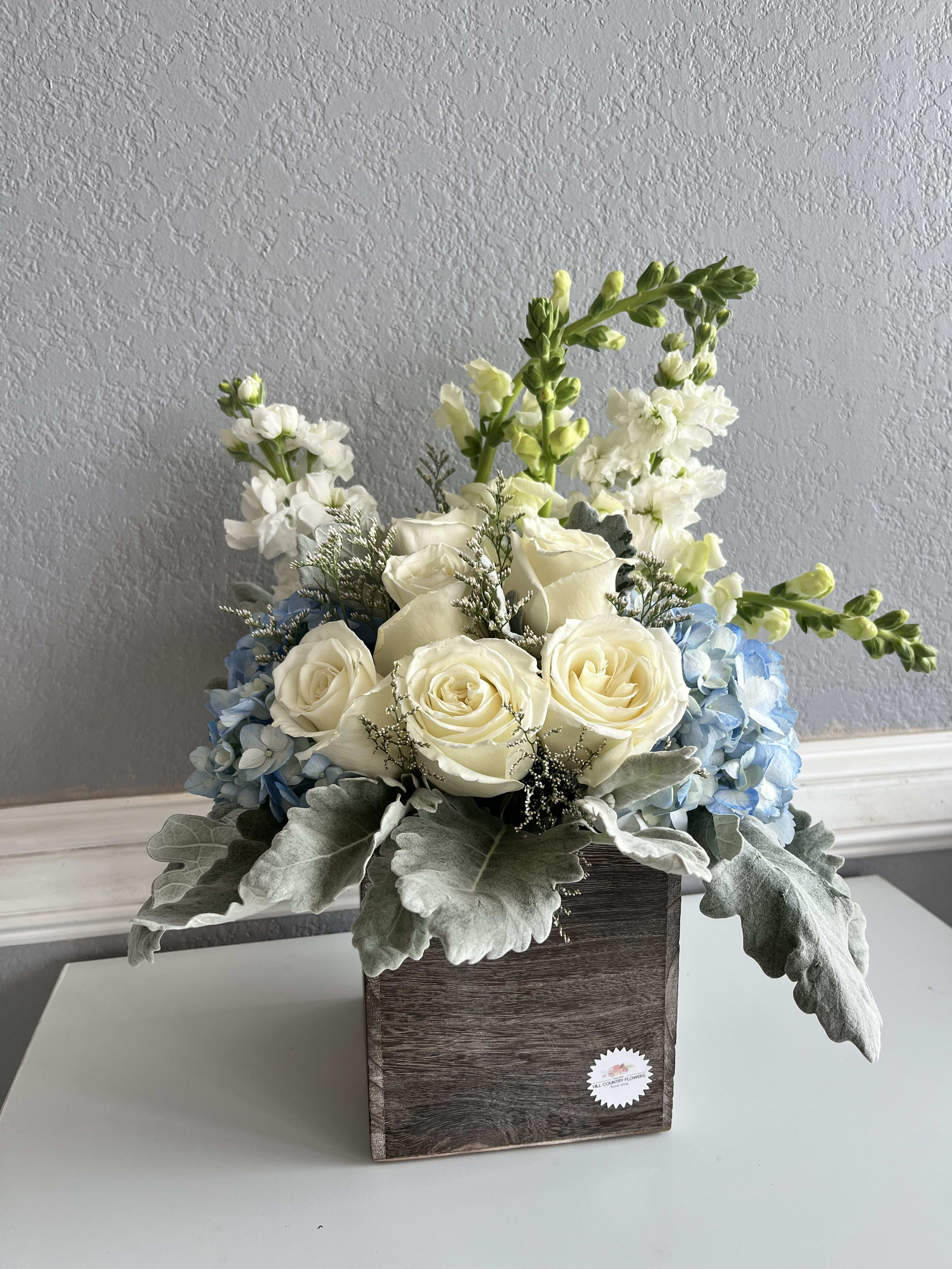White roses and blue hydrangeas in a wooden box with tall white blooms