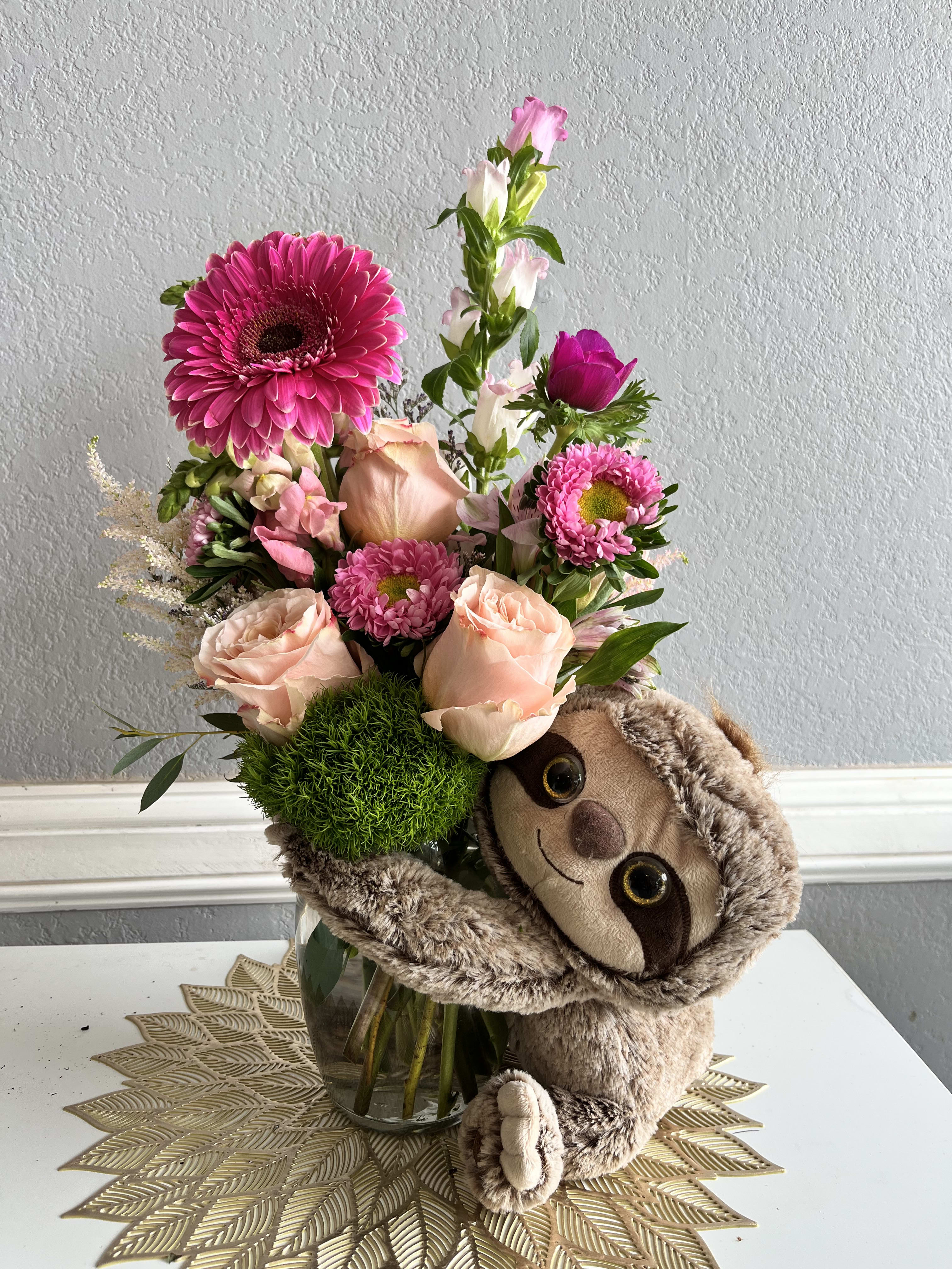 Pink flower arrangement with a plush sloth in a glass vase