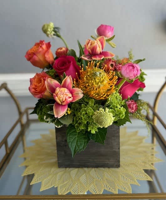 Mixed bouquet in a dark square vase with pink, orange, and green blooms