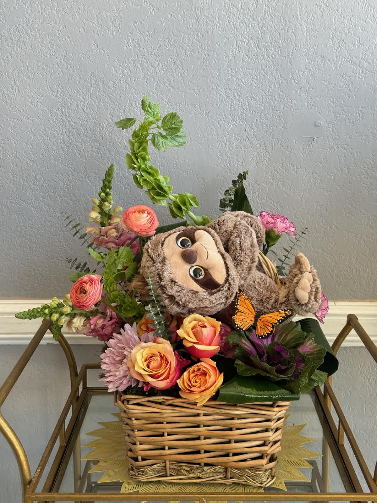 Basket arrangement with roses, mixed flowers, and a plush sloth
