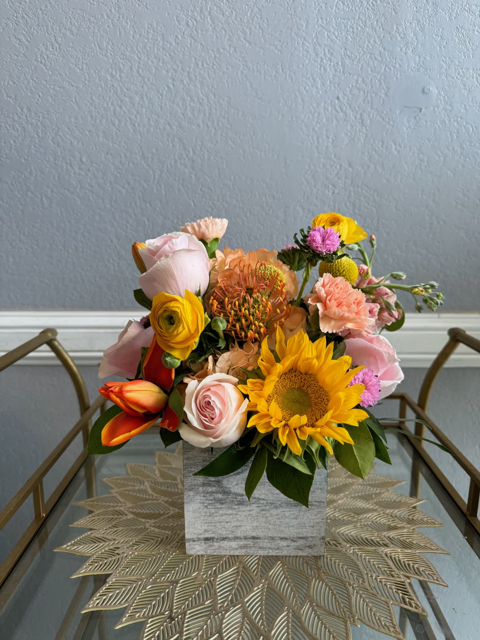 Mixed bouquet with sunflowers, roses, and carnations in a square vase