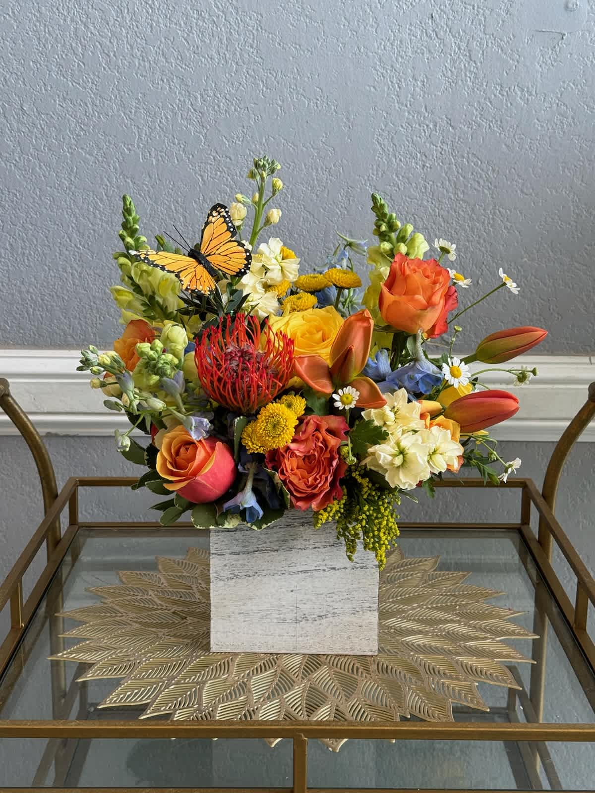 Mixed bouquet of orange, yellow, and white flowers in a square vase