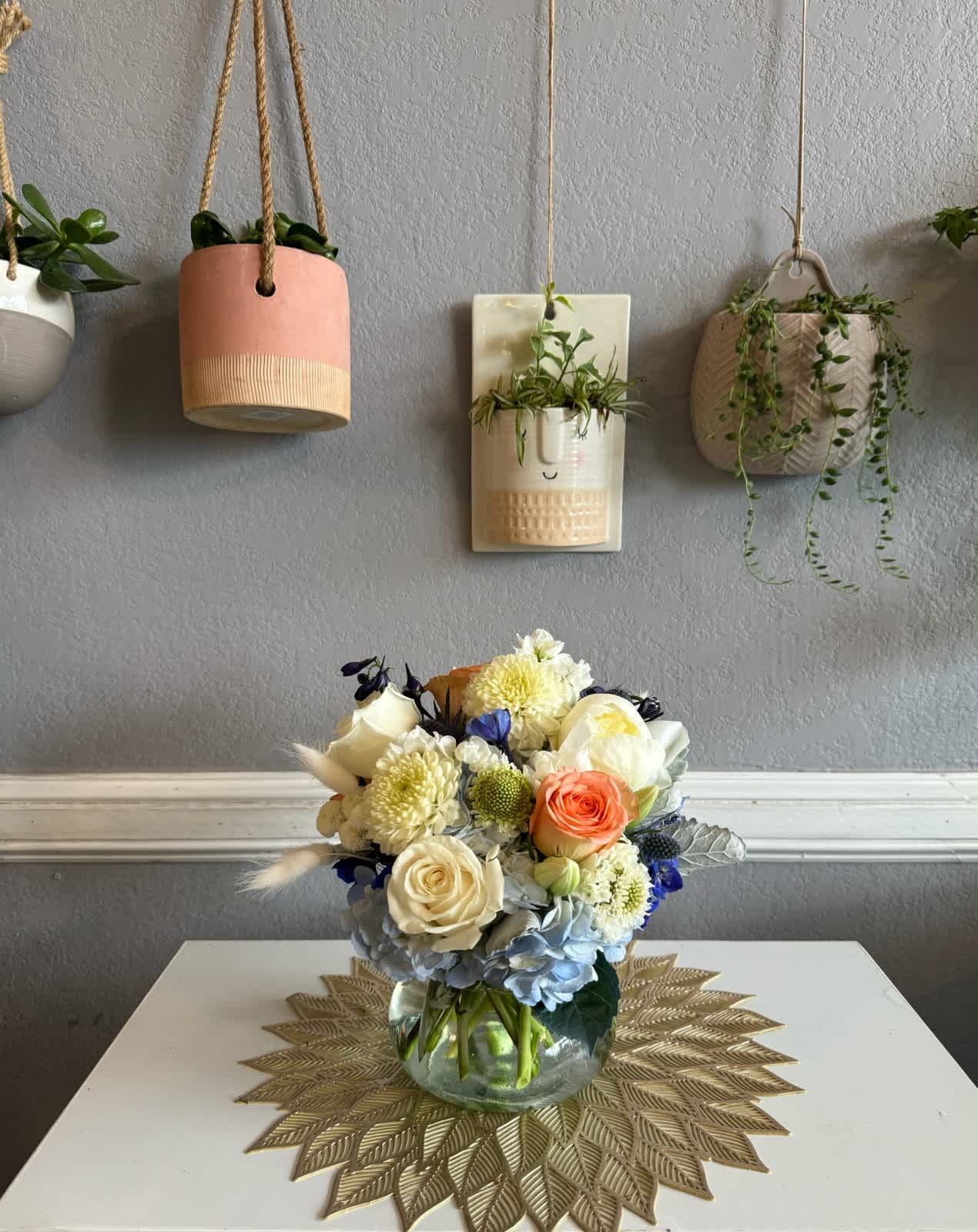 Mixed bouquet in a clear glass vase with cream, peach, blue, and yellow flowers.