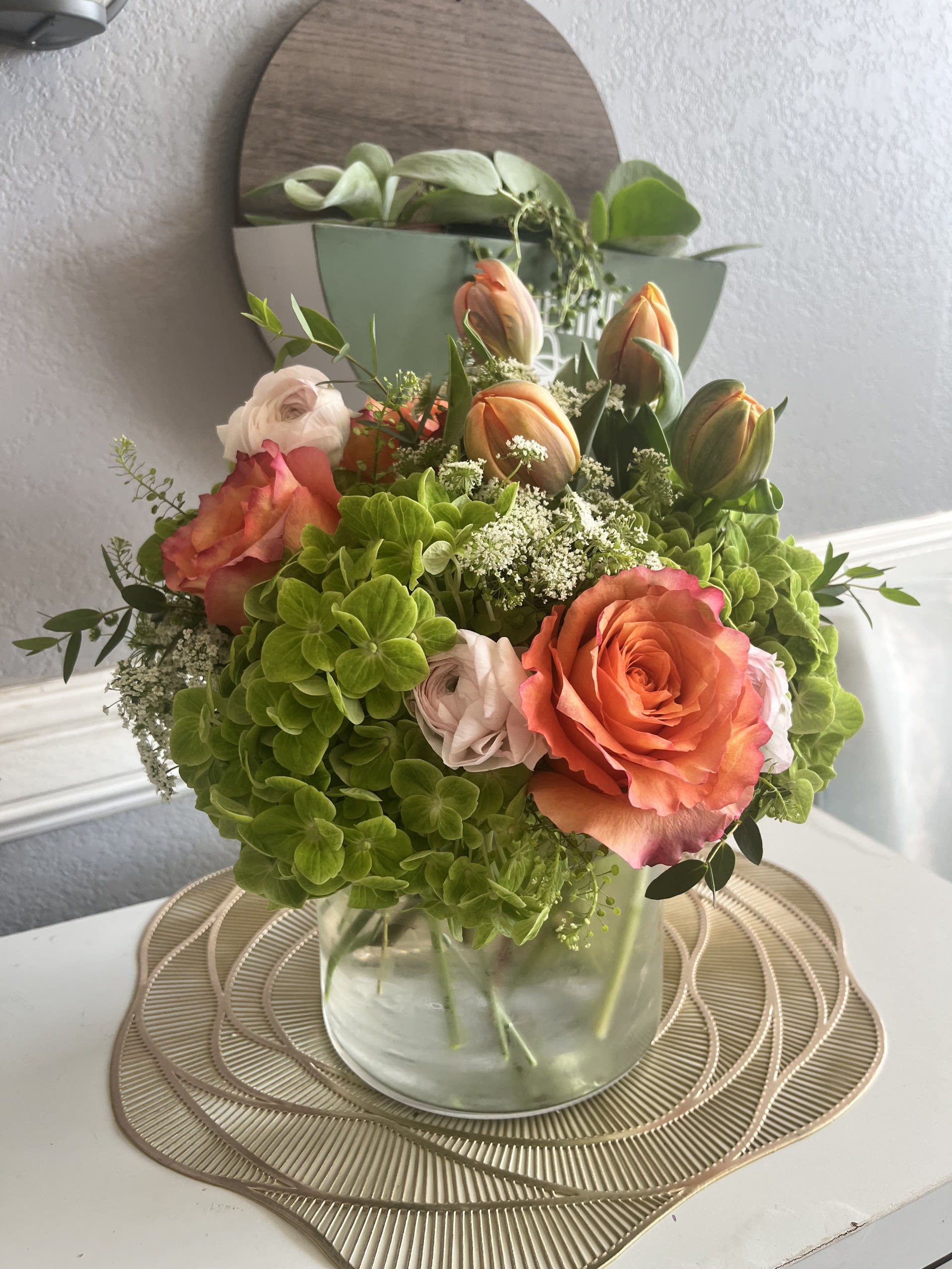 Bouquet of orange roses, green hydrangeas, and tulips in a glass vase