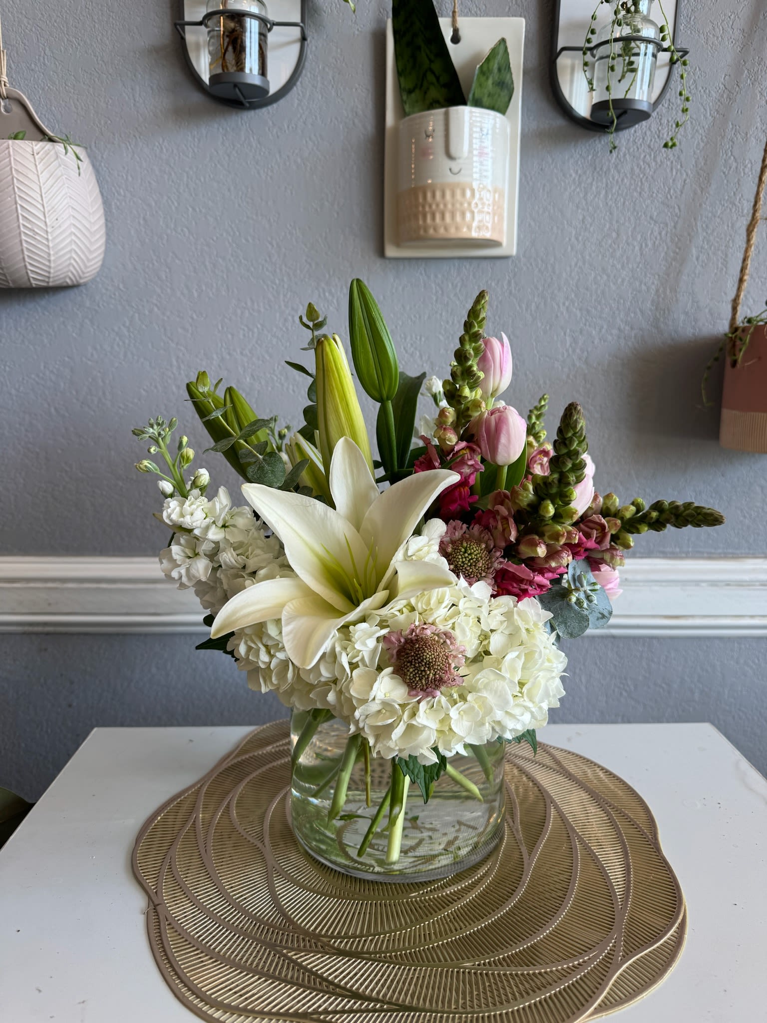 Mixed bouquet with white lilies, hydrangeas, and pink blooms in a glass vase
