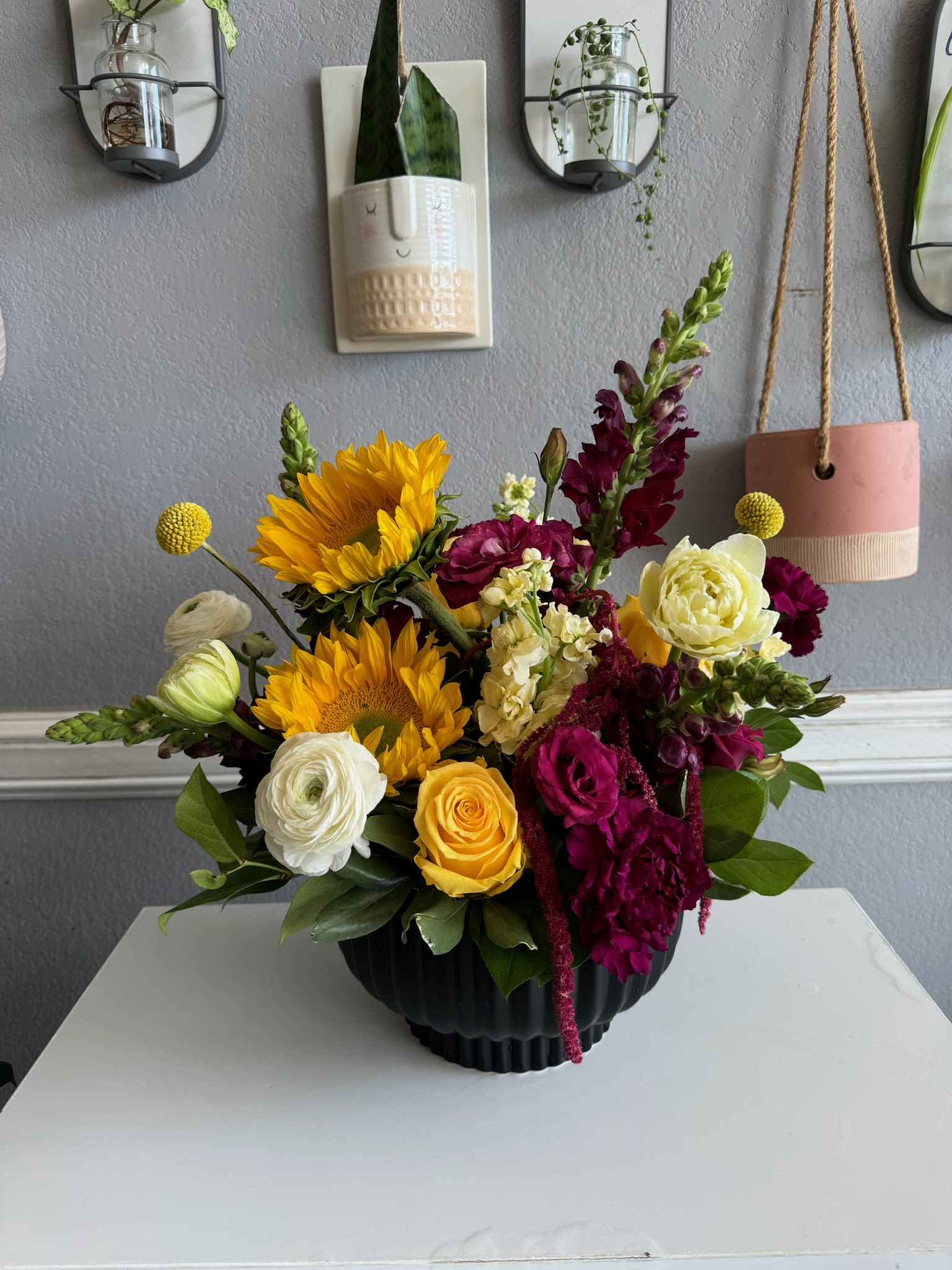 Mixed bouquet with sunflowers, roses, and snapdragons in a black vase