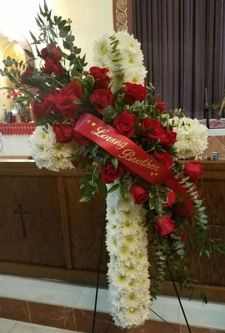 Elegance &amp; Sophistication Cross Spray - This elegant heart-shaped standing spray is a loving tribute, beautifully crafted with radiant red roses and graceful white Fuji mums. Its bold, classic color palette and striking shape symbolize deep love, devotion, and remembrance. Designed on a standing cross easel, this large floral display offers a meaningful expression of sympathy and heartfelt honor for a cherished loved one.  Please note: Floral variety may vary based on seasonal availability, ensuring each arrangement is fresh and unique.