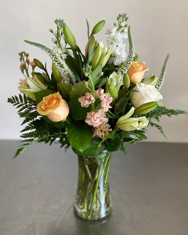 Tall bouquet of peach roses, white lilies, and soft pink flowers in a clear glass vase
