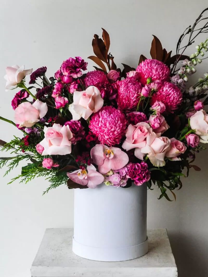 Pink and magenta floral arrangement in a white cylindrical vase