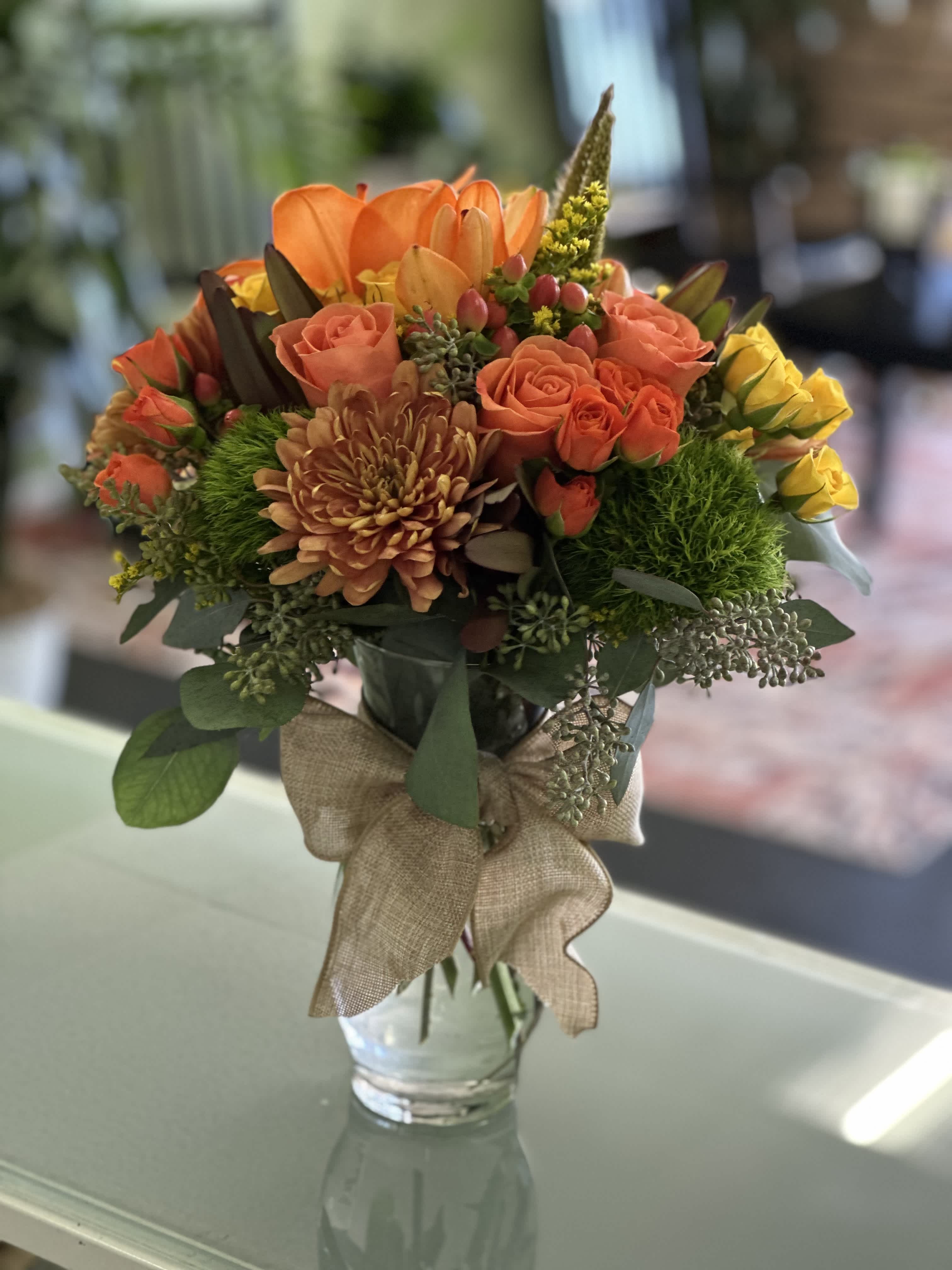 Orange and yellow bouquet in a glass vase with a burlap ribbon