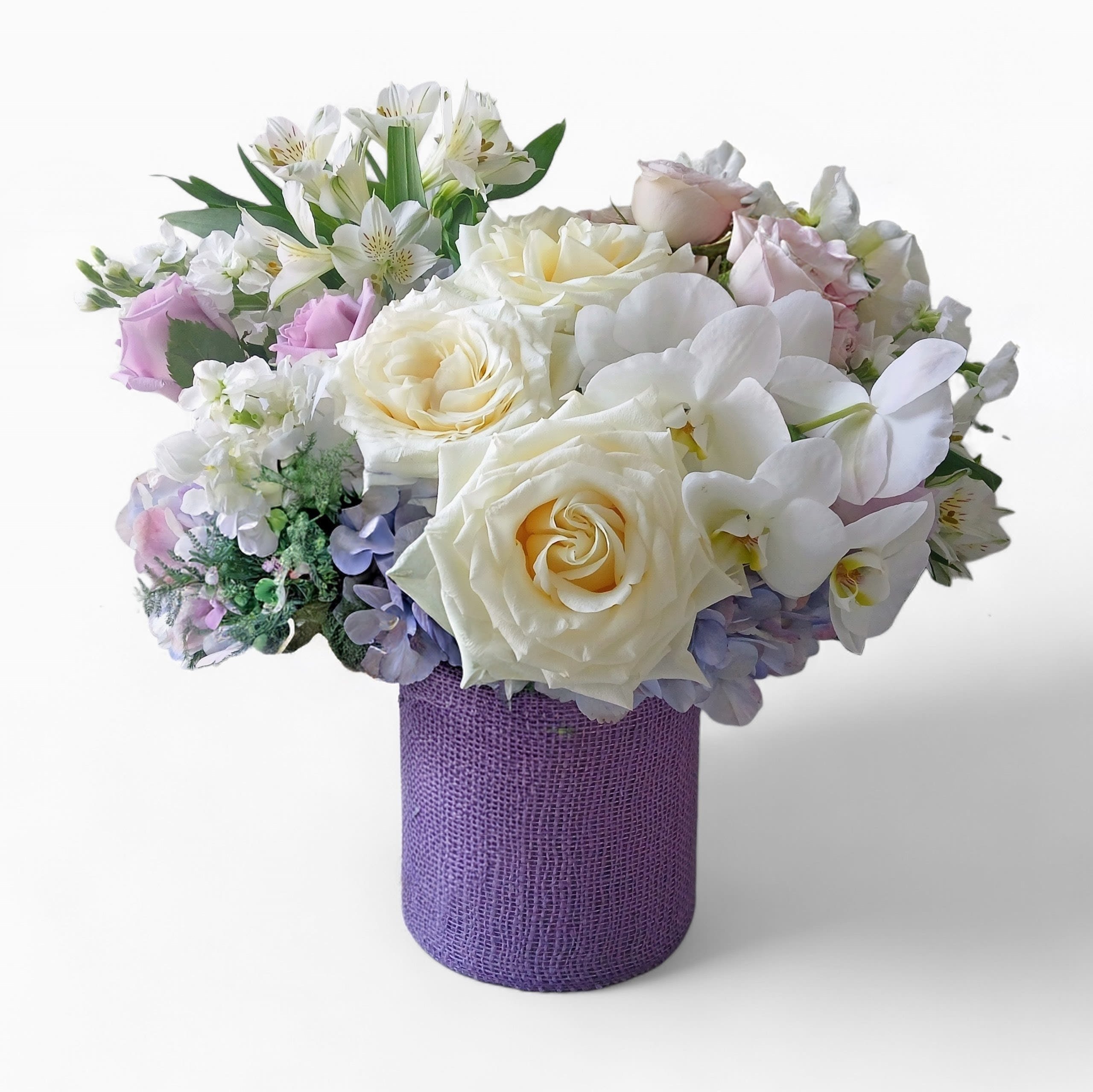 Low round arrangement of white and pastel flowers in a textured purple cylinder vase