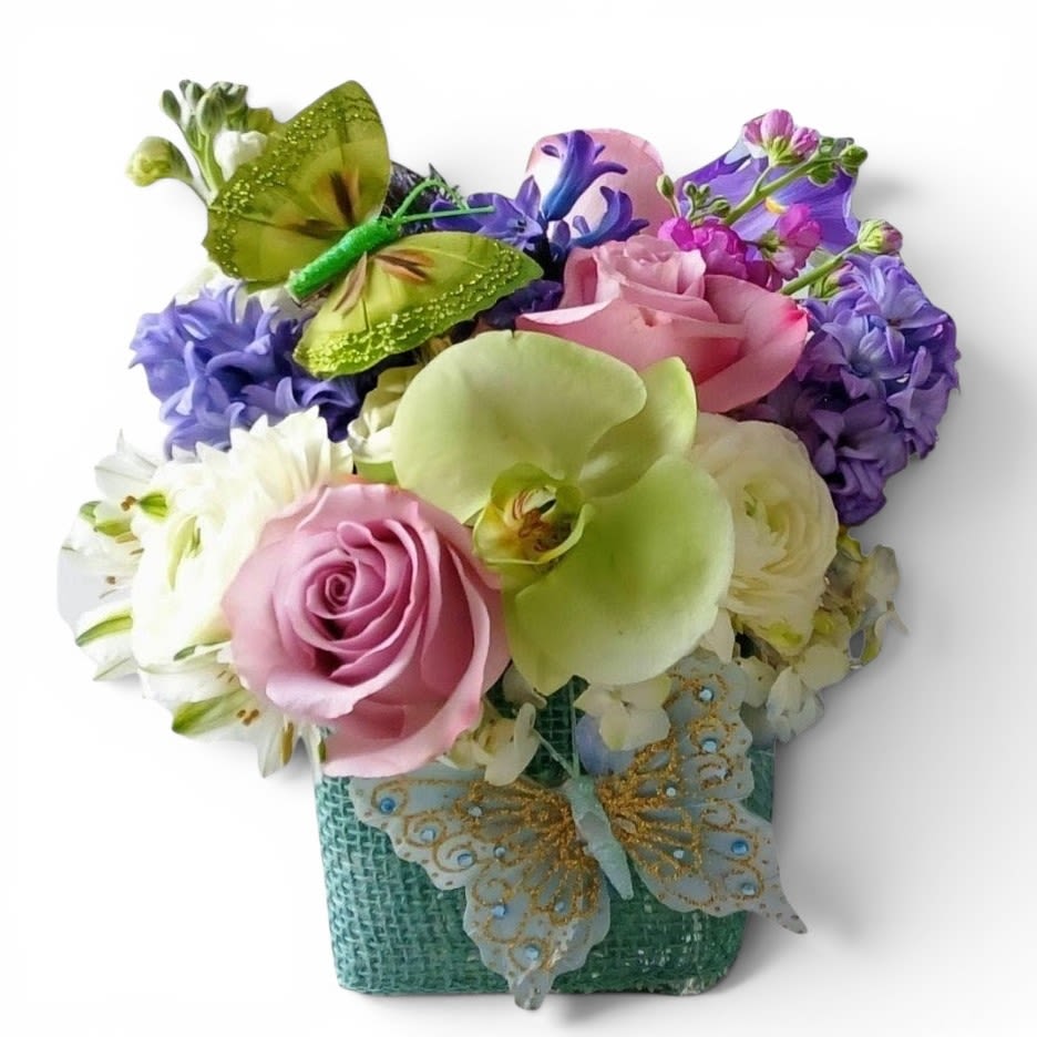 Vanilla Blue Blossoms Designer's Choice - Send this beauty today to make them smile with it's lovely mix vanilla and blue blossoms of the day roses hydrangeas and more arranged in a modern glass cube vase wrapped in pretty blue jute ribbon. Beautiful. Always made extra special and unique. Send them happiness.