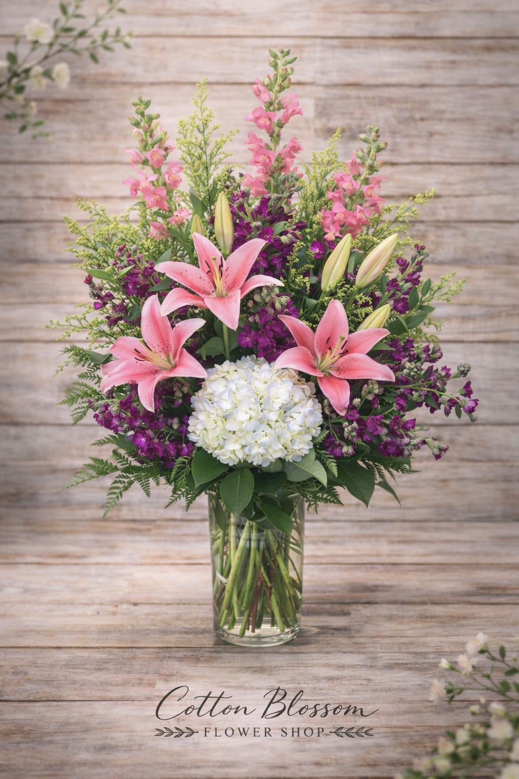 Pink lilies and purple flowers arranged in a glass vase with white hydrangea