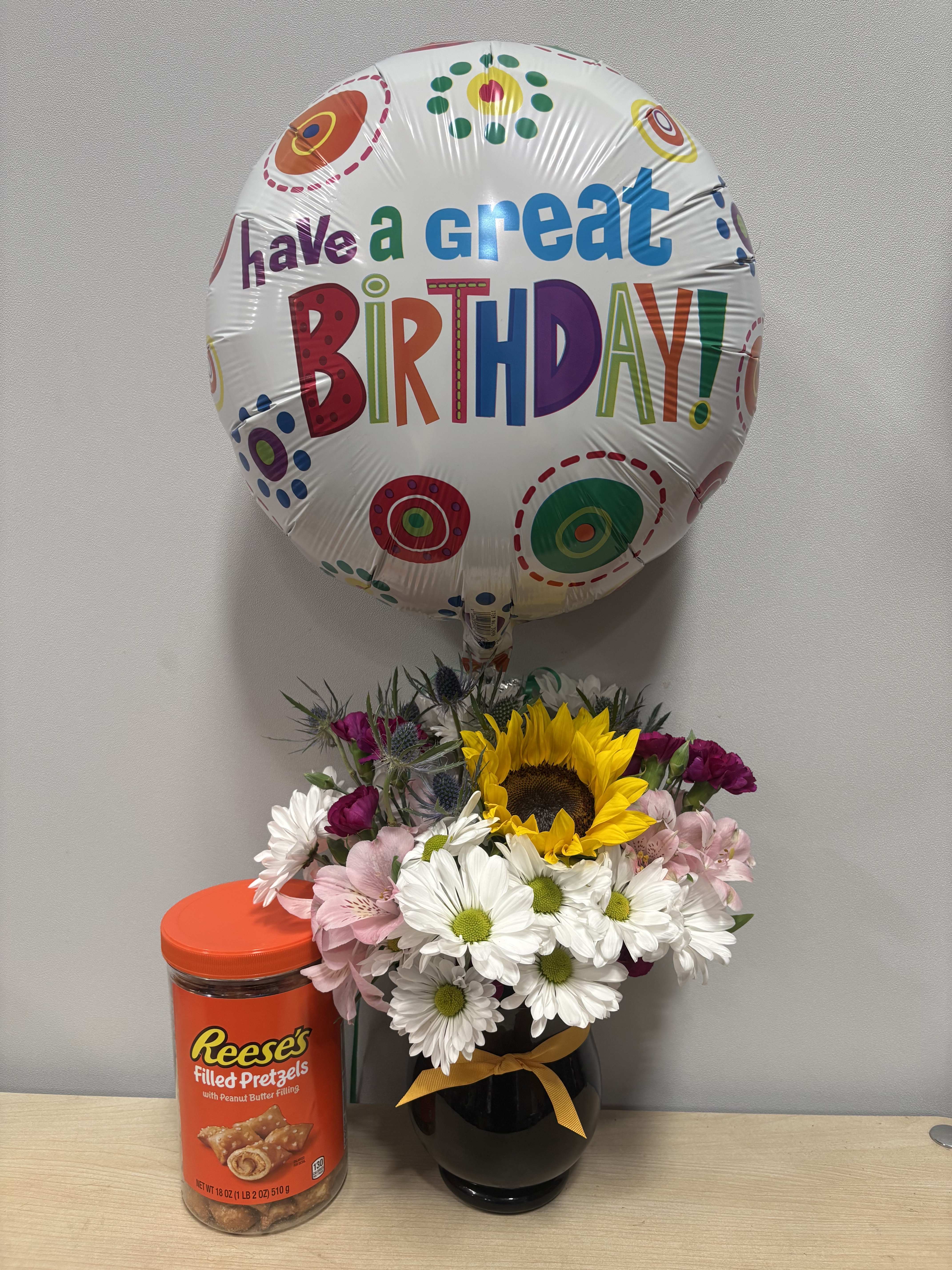 Birthday balloon above a mixed flower arrangement with a candy container