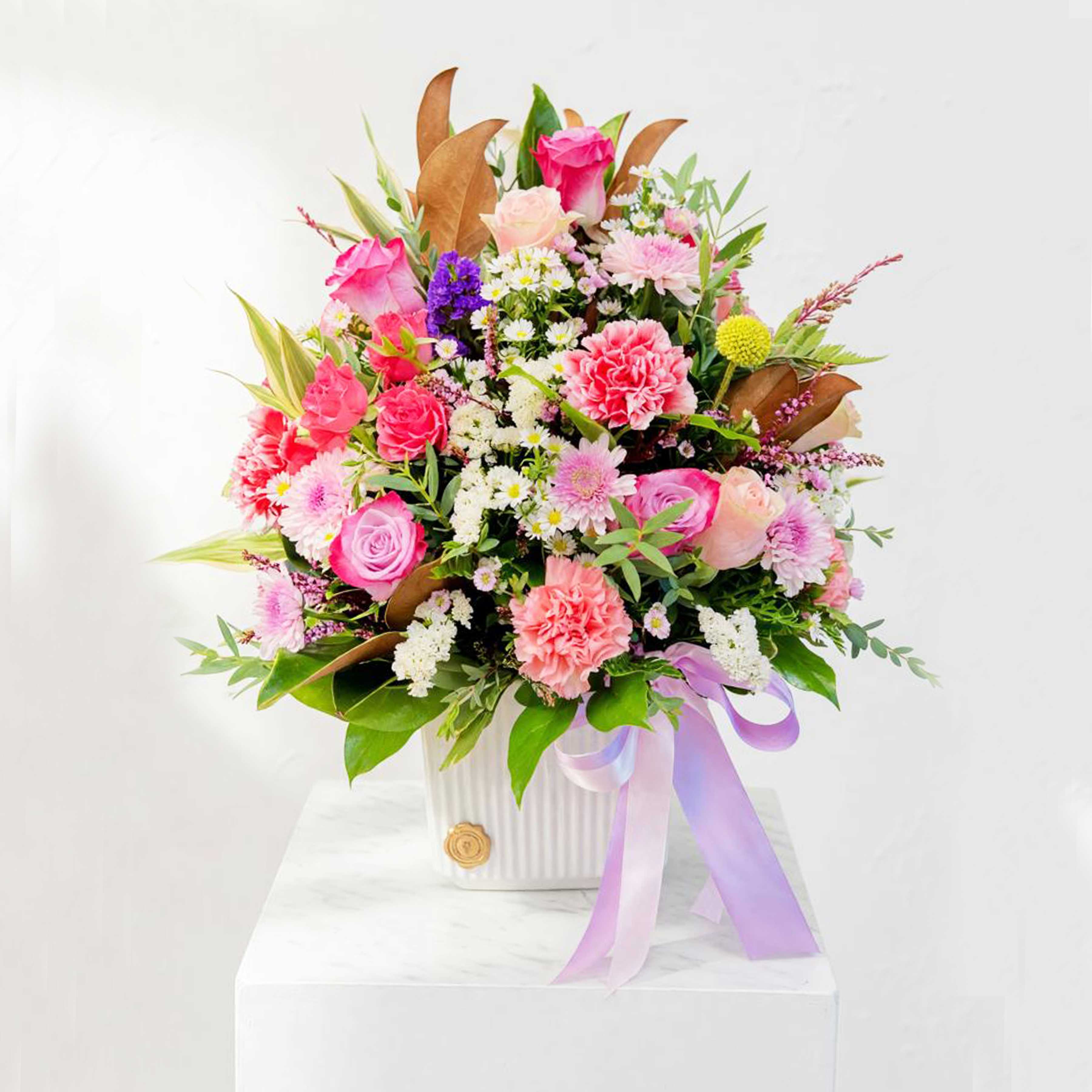 Mixed pink and white flower arrangement in a white vase with a lavender ribbon
