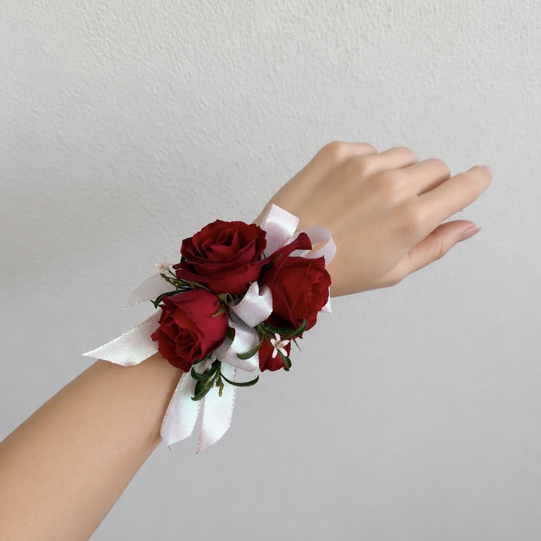 Red rose wrist corsage with white ribbon on a hand