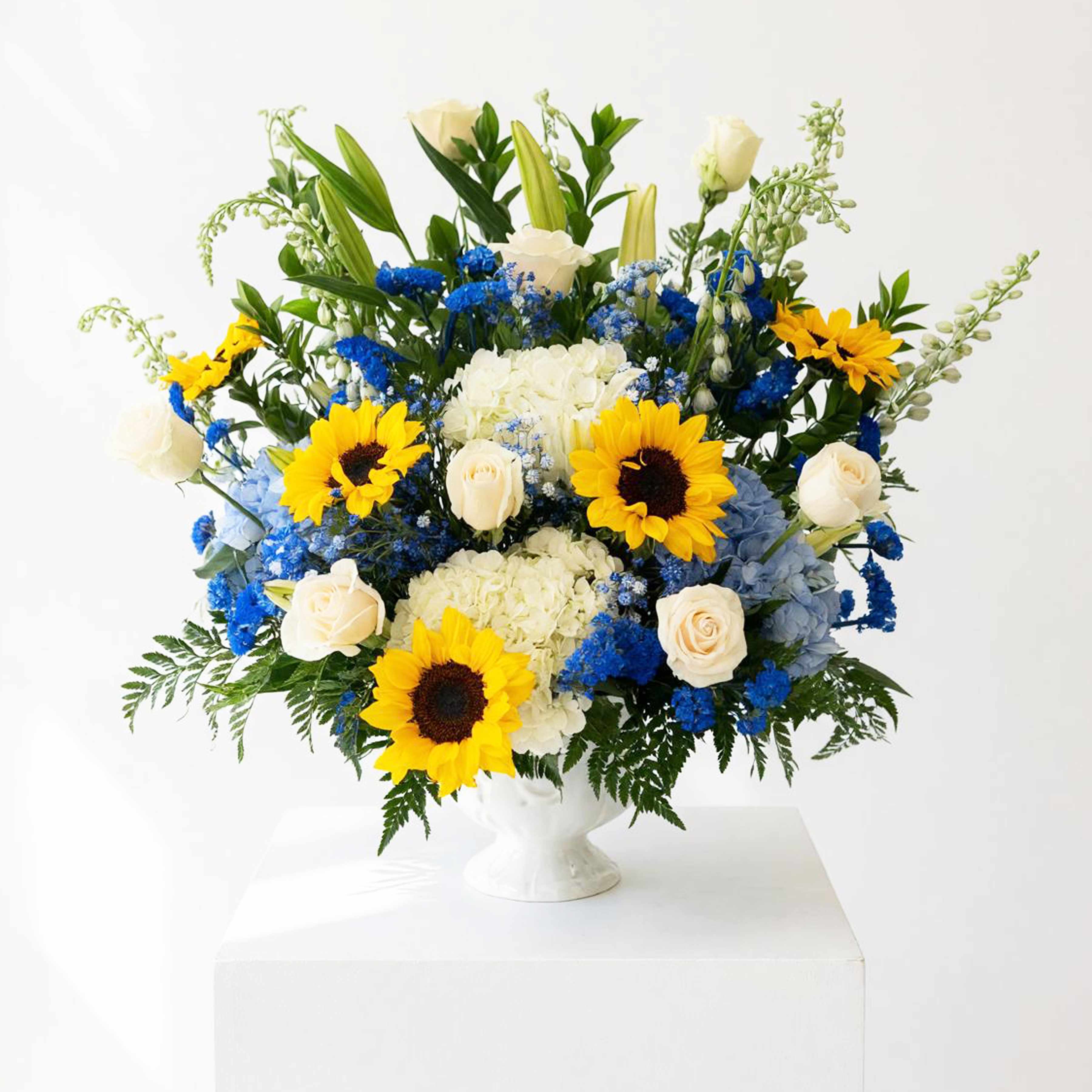 Large bouquet of sunflowers, white roses, and blue flowers in a white vase
