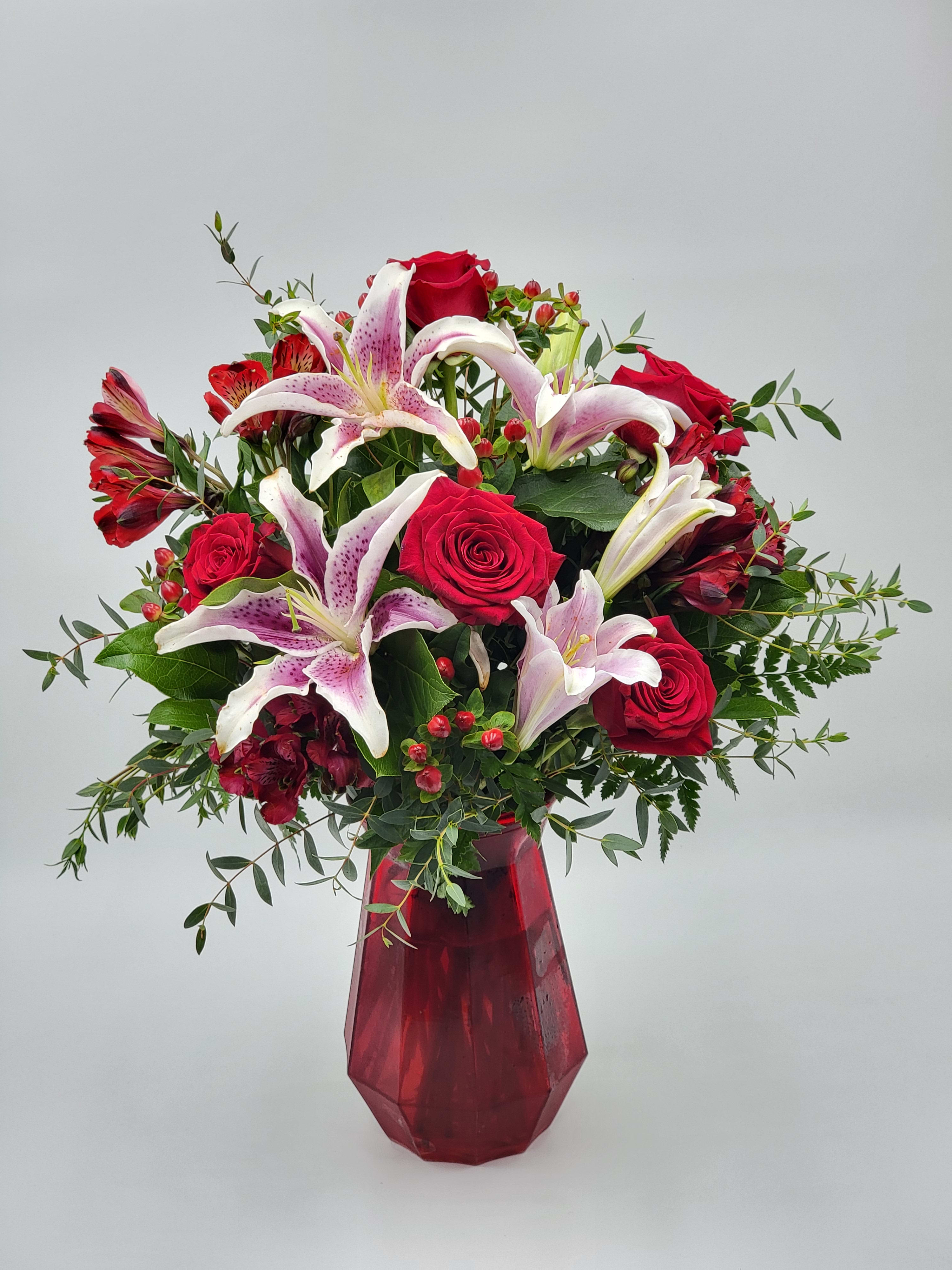 Bouquet of red roses and pink lilies in a red glass vase