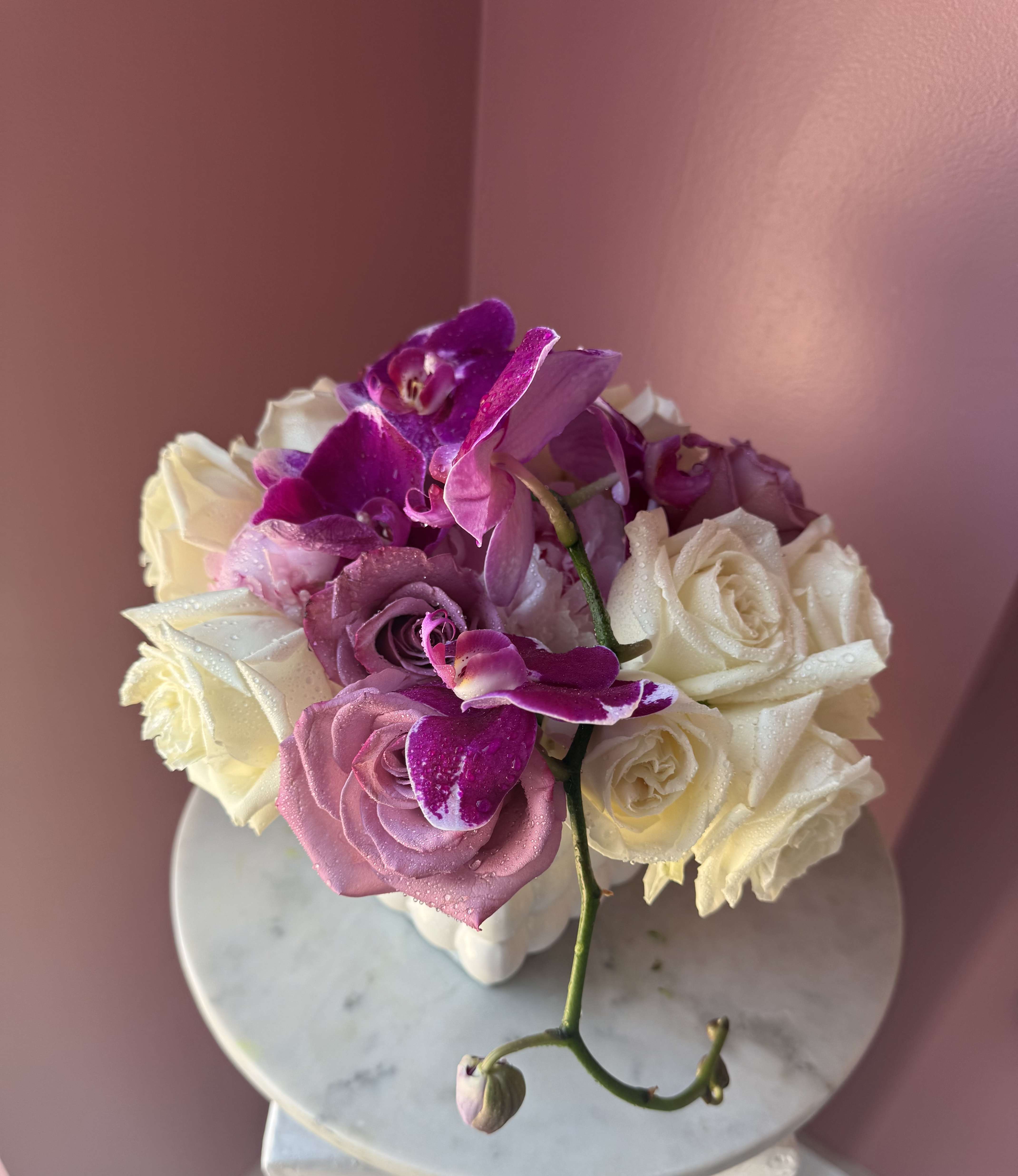 Pink and white roses with purple orchids in a white vase