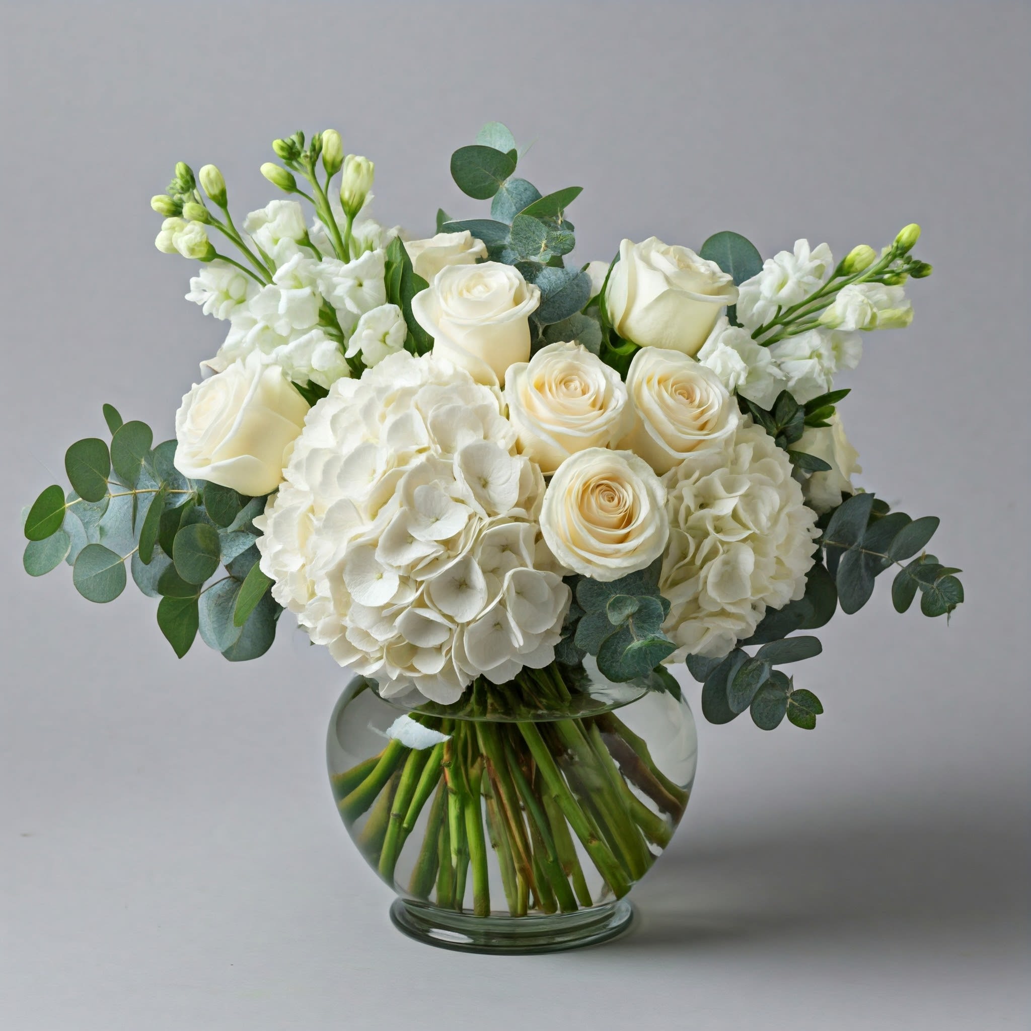 White roses and hydrangeas in a round glass vase with eucalyptus