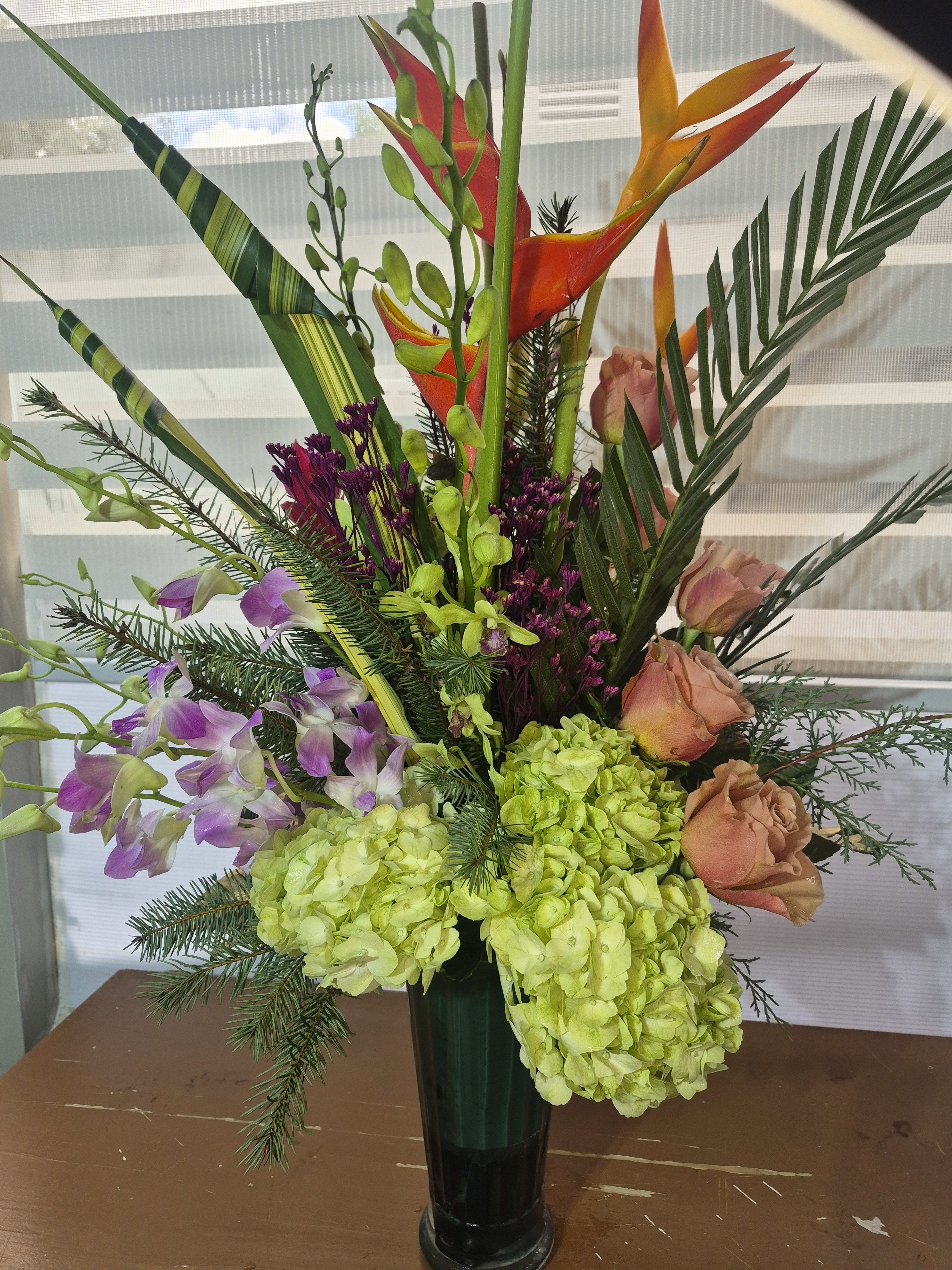 TROPICAL SERENADE - AN ALL AROUND ARRANGEMENT CONSISTING OF WHITE/GREEN HYDRANGIAS, LAVENDER/WHITE DENDROBRIUM ORCHIDS, PEACH ROSES, ALACONIAS AND AN ASSORTMENT OF TROPICAL GREENS/FOLIAGE