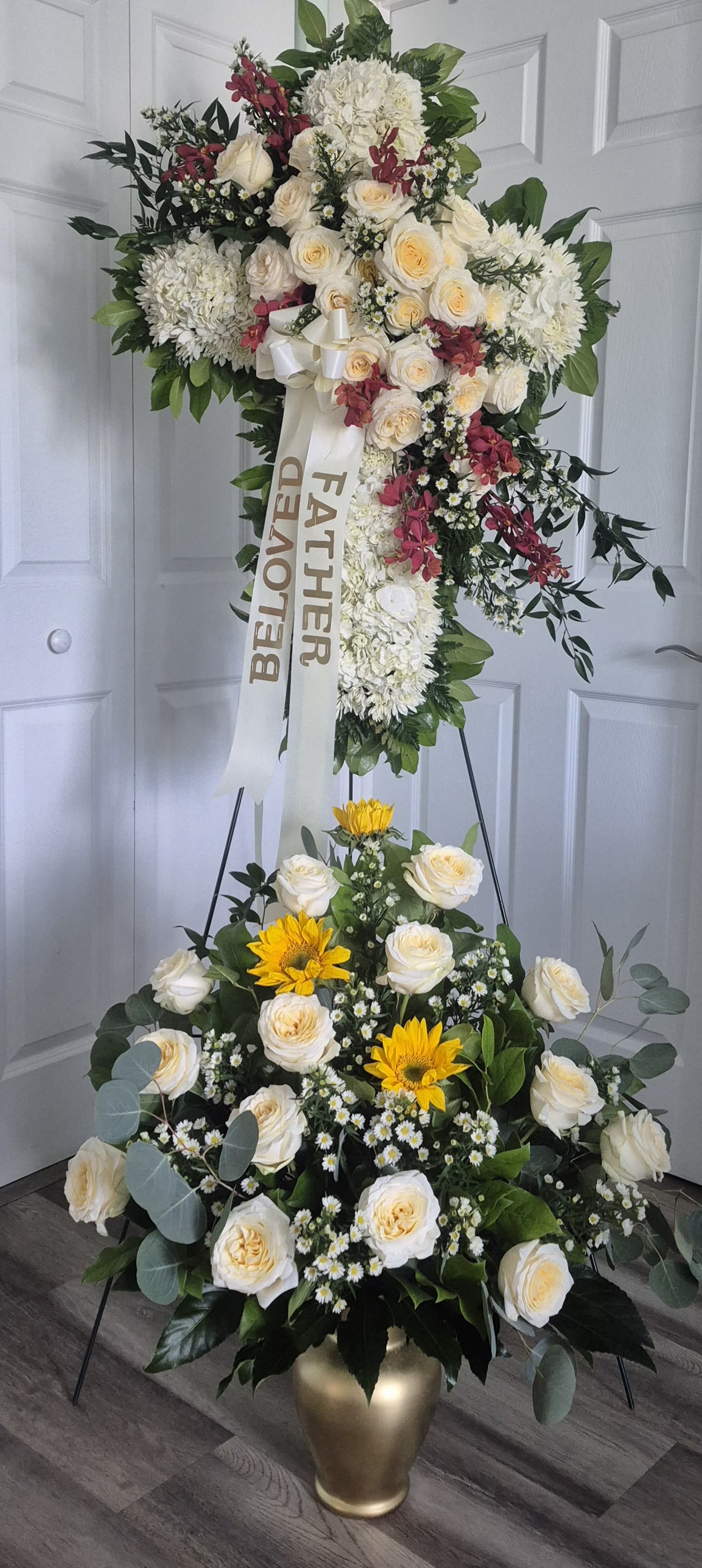 SYMPATHY CROSS BUNDLE - A SIX FOOT (6FT) TALL SYMPATHY CROSS SONSISTING OF WHITE MUMMS BLOSSOMS, WHITE ROSES, WHITE MONTI-CASINO FILLER AND RED MOKARA ORCHIDS. ACCOMPANIED WITH A 3FT TALL ONE-SIDED ARRANGEMENT IN AN URN SHAPED VASE THAT HAS WHITE ROSES AND YELLOW SUNFLOWERS. 