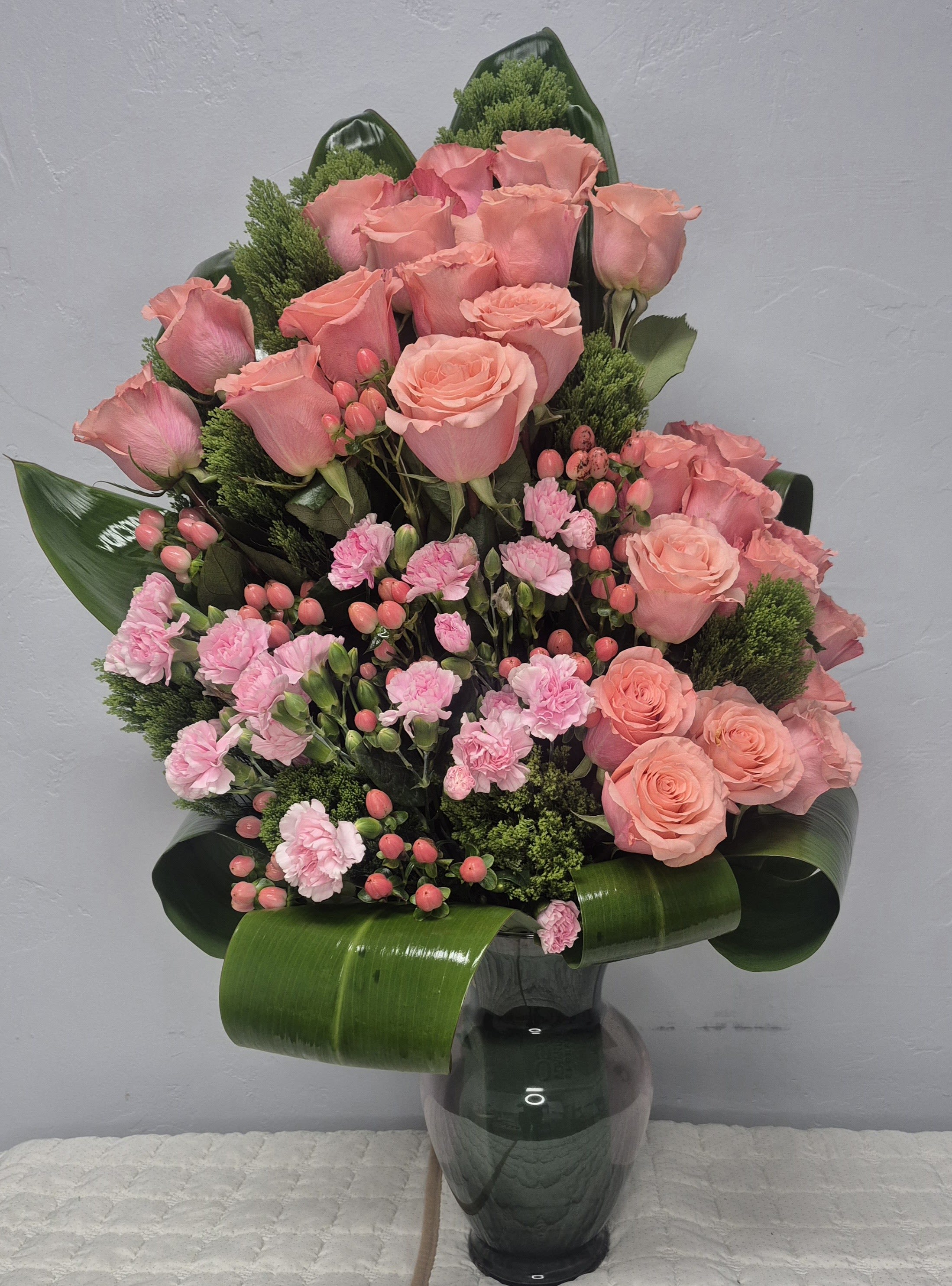 PINK DEVOTION - PINK ROSES, PINK CARNATIONS, PINK/PEACH HYPERICUM BERRIES, DIANTHUS FLOWERS, AND TALL TI LEAVES ARRANGED ONESIDED IN A 11 INCHES GLASS VASE.