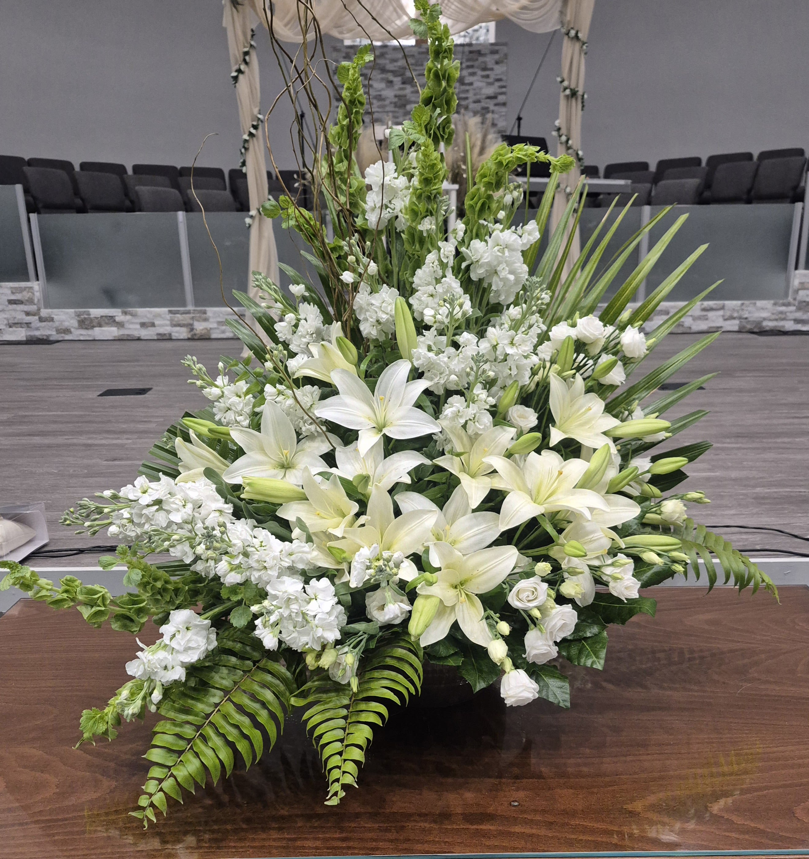Large white floral arrangement with lilies and greenery in a church setting