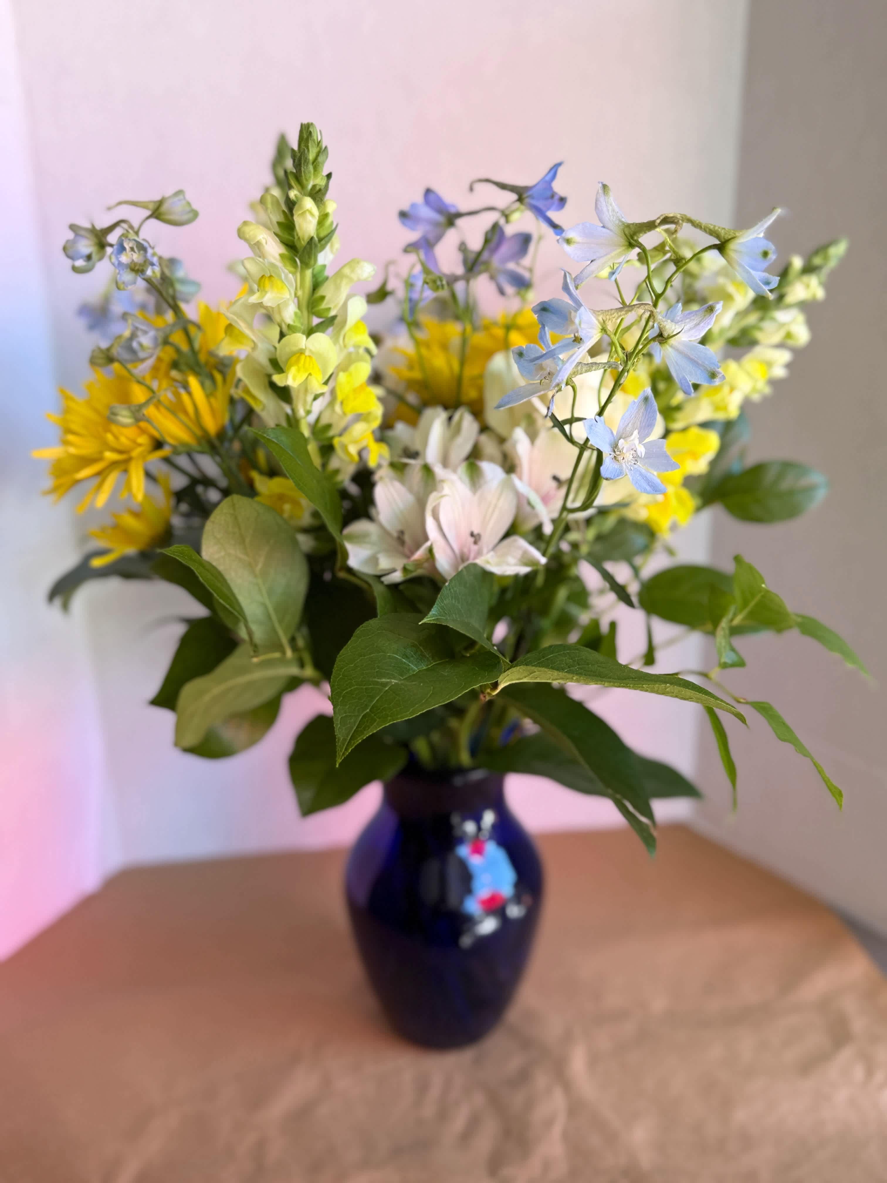 Mixed bouquet of yellow, blue, and pale pink flowers in a dark vase