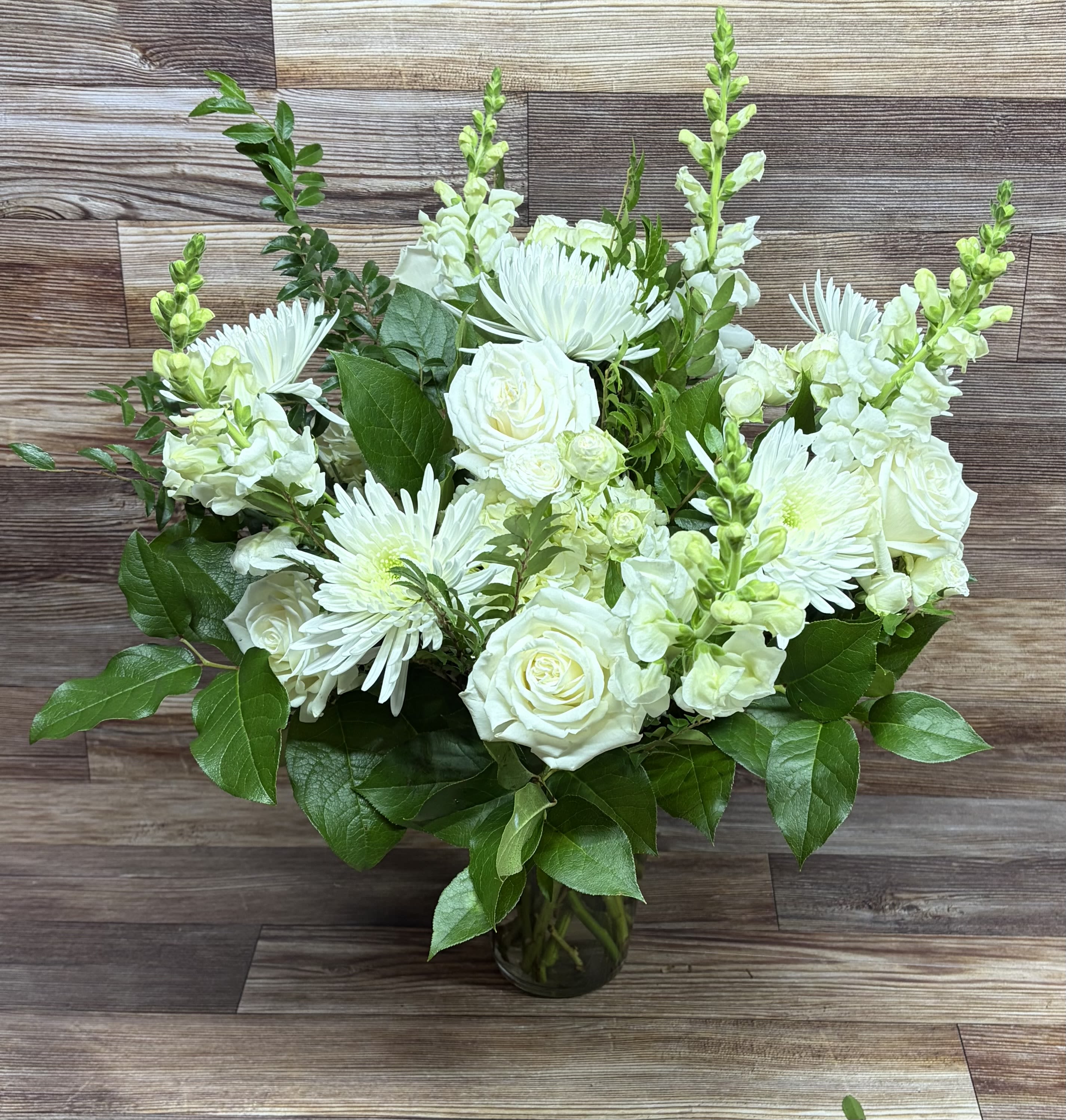 Arrangement of white roses, chrysanthemums, and snapdragons in a clear glass vase